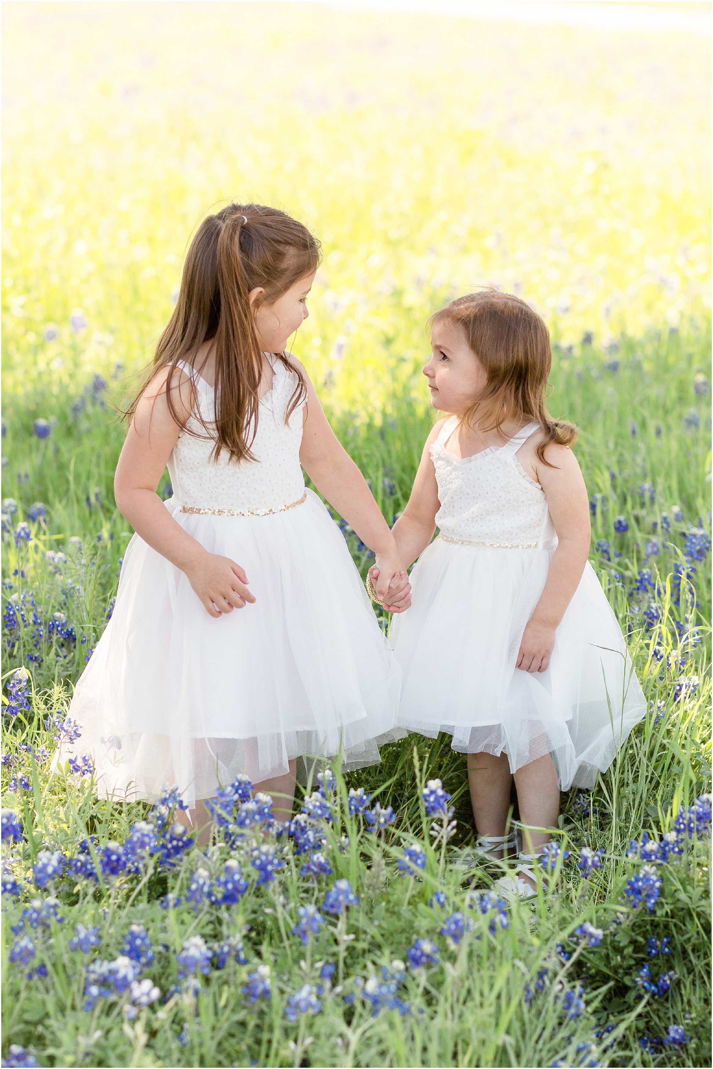 sisters in white dresses in a bluebonnet field