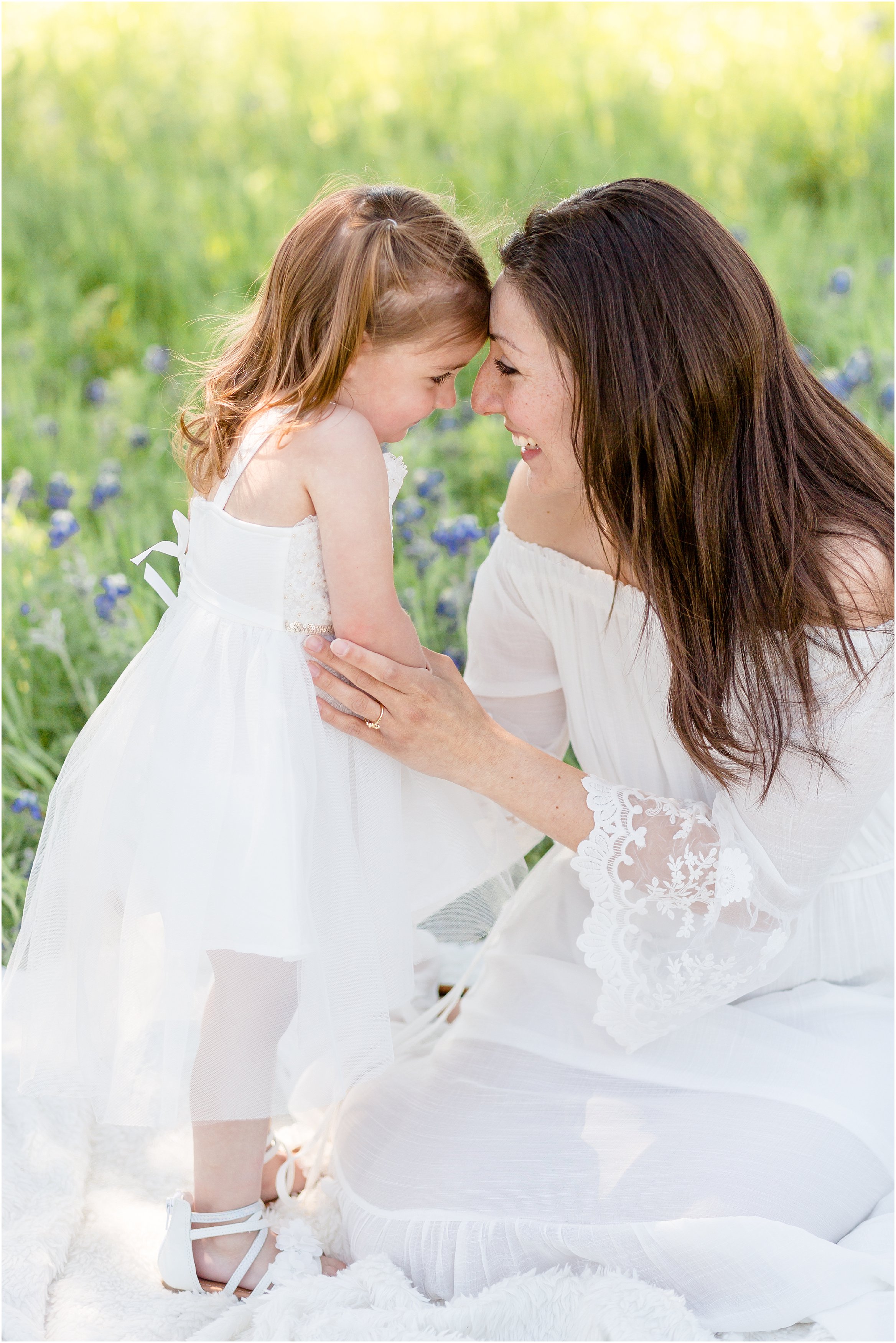 mom and daughter in white dresses in a bluebonnet field