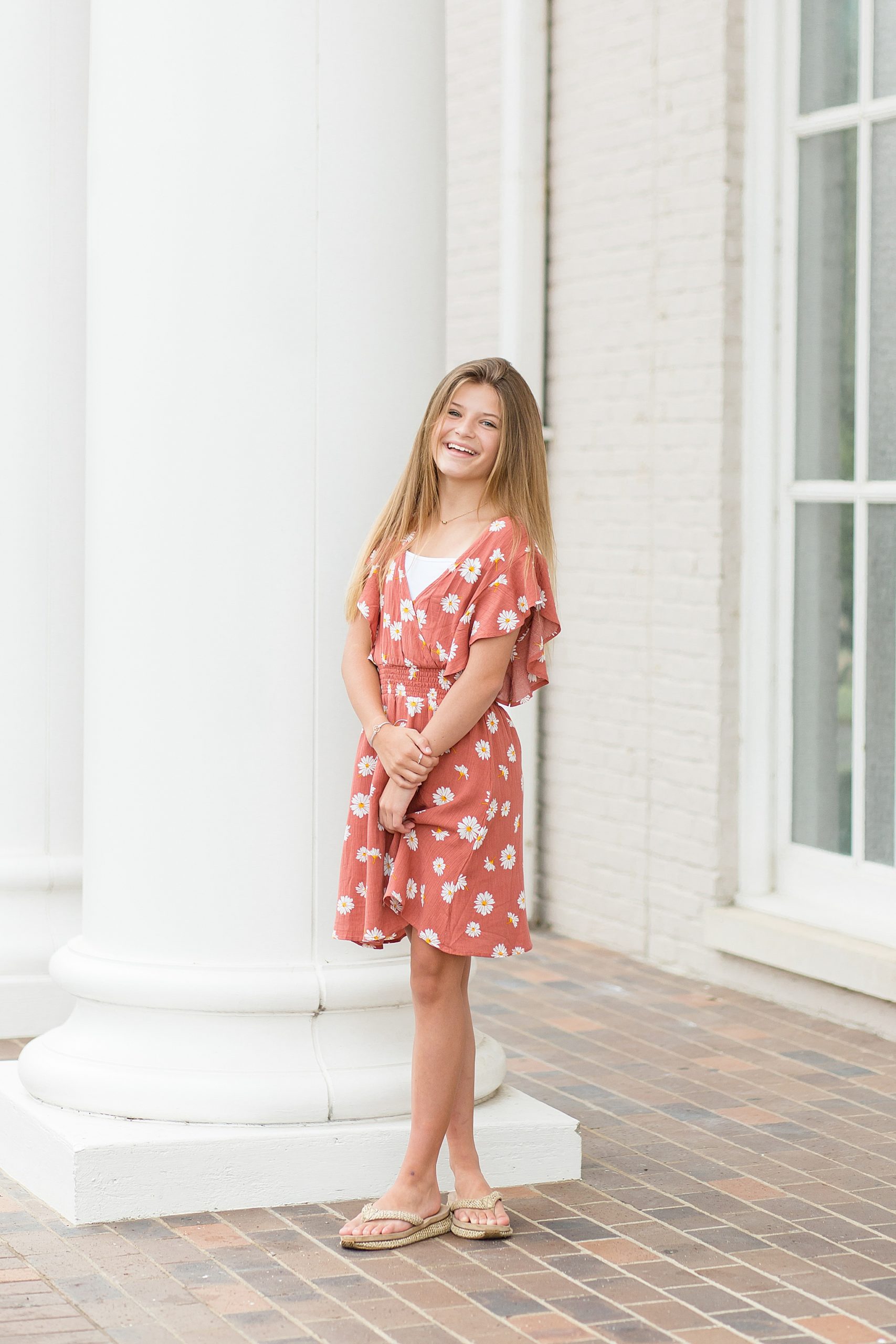 teenager in floral dress smiles by pillar