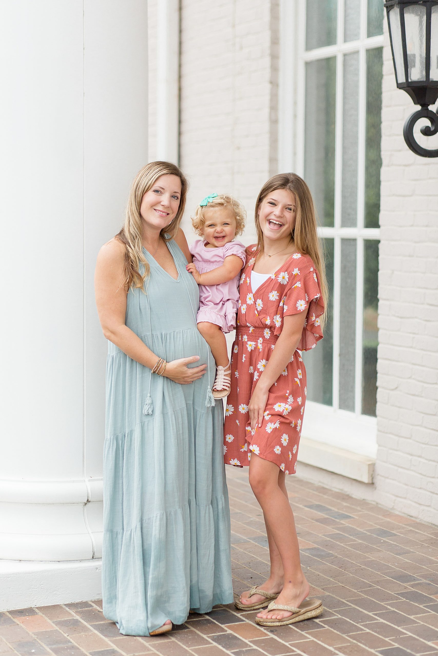 mom, toddler and daughter pose while mom holds belly