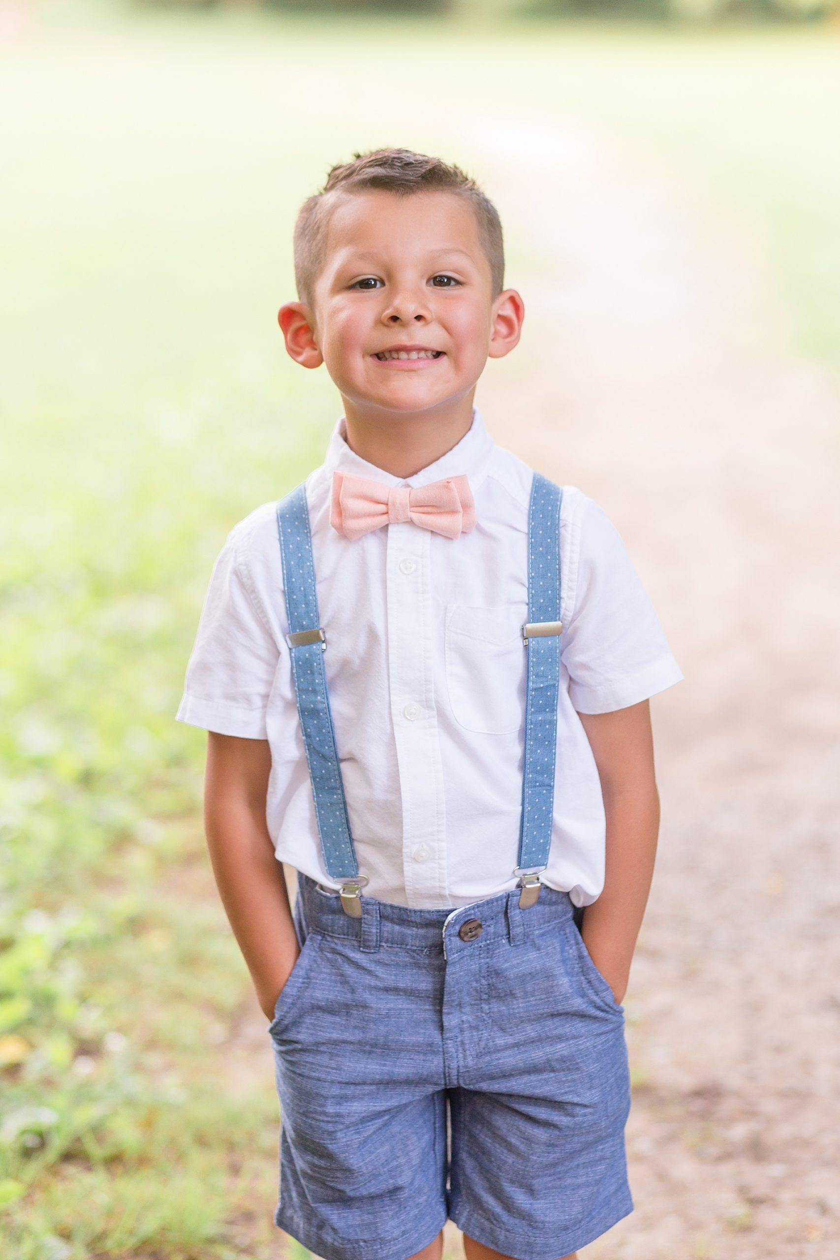 boy in blue suspenders with pink bowtie smiles during Pinkerton Park family portraits
