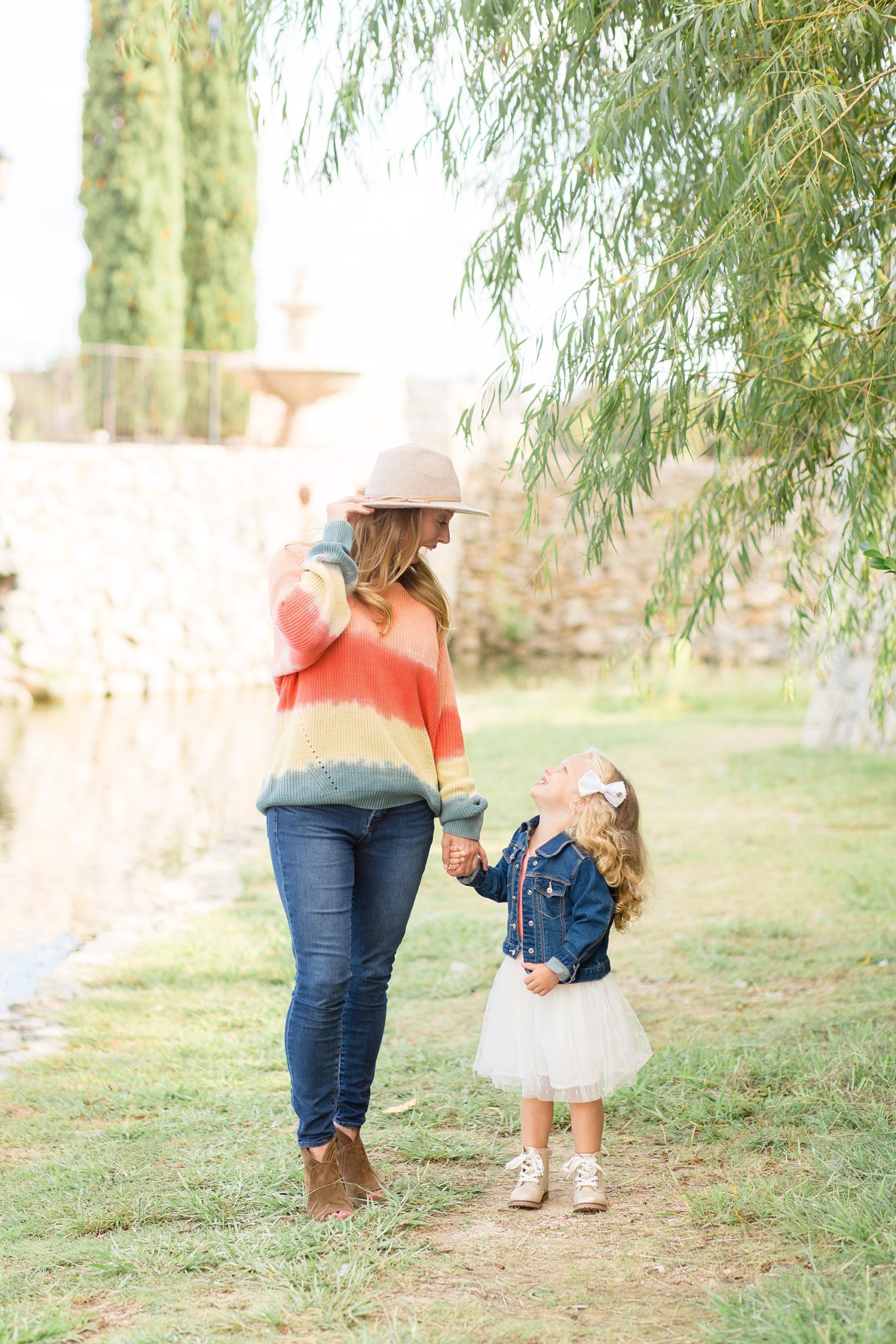 mom in floppy hat poses with toddler daughter in jean jacket