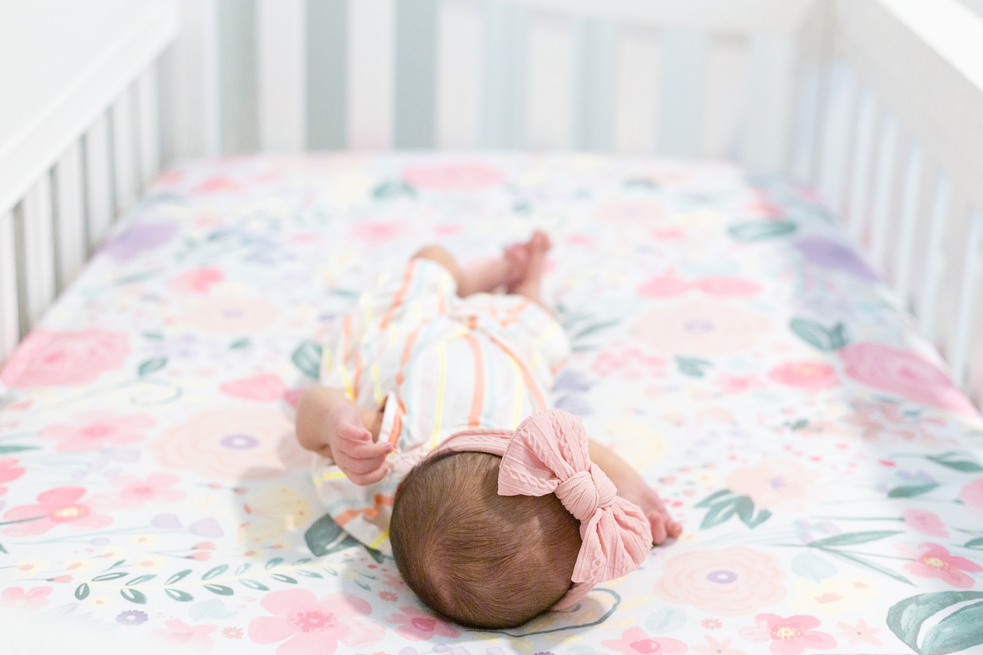 baby girl with pink bow lays in crib