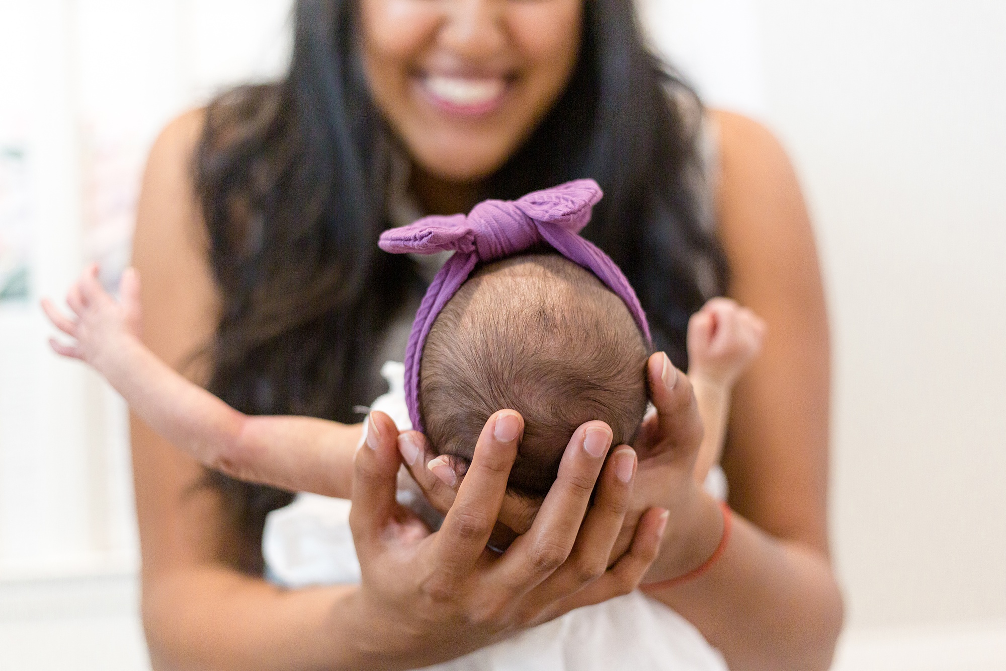 mom holds baby girl in purple bow by crib