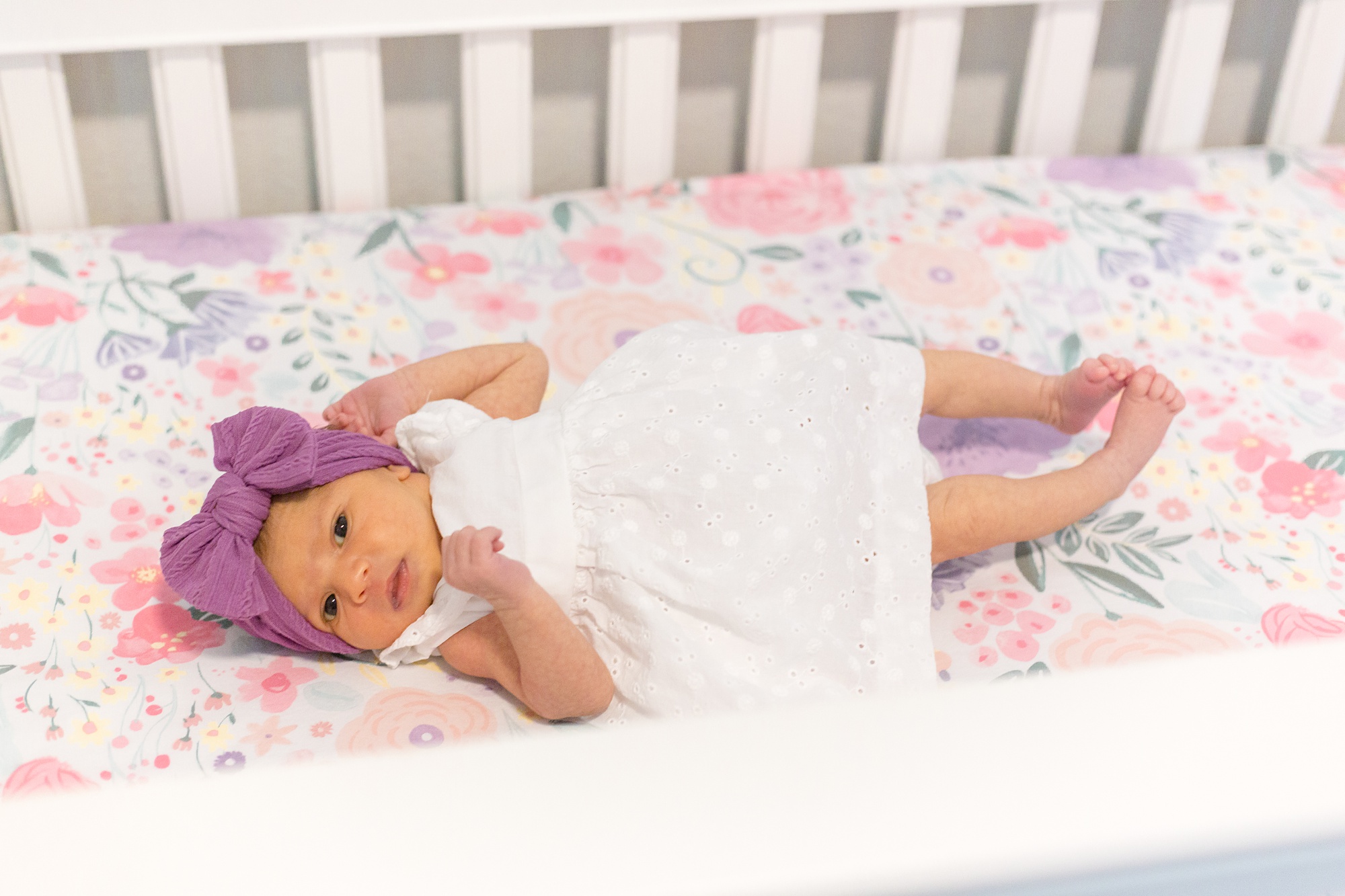 baby girl lays in crib with purple bow