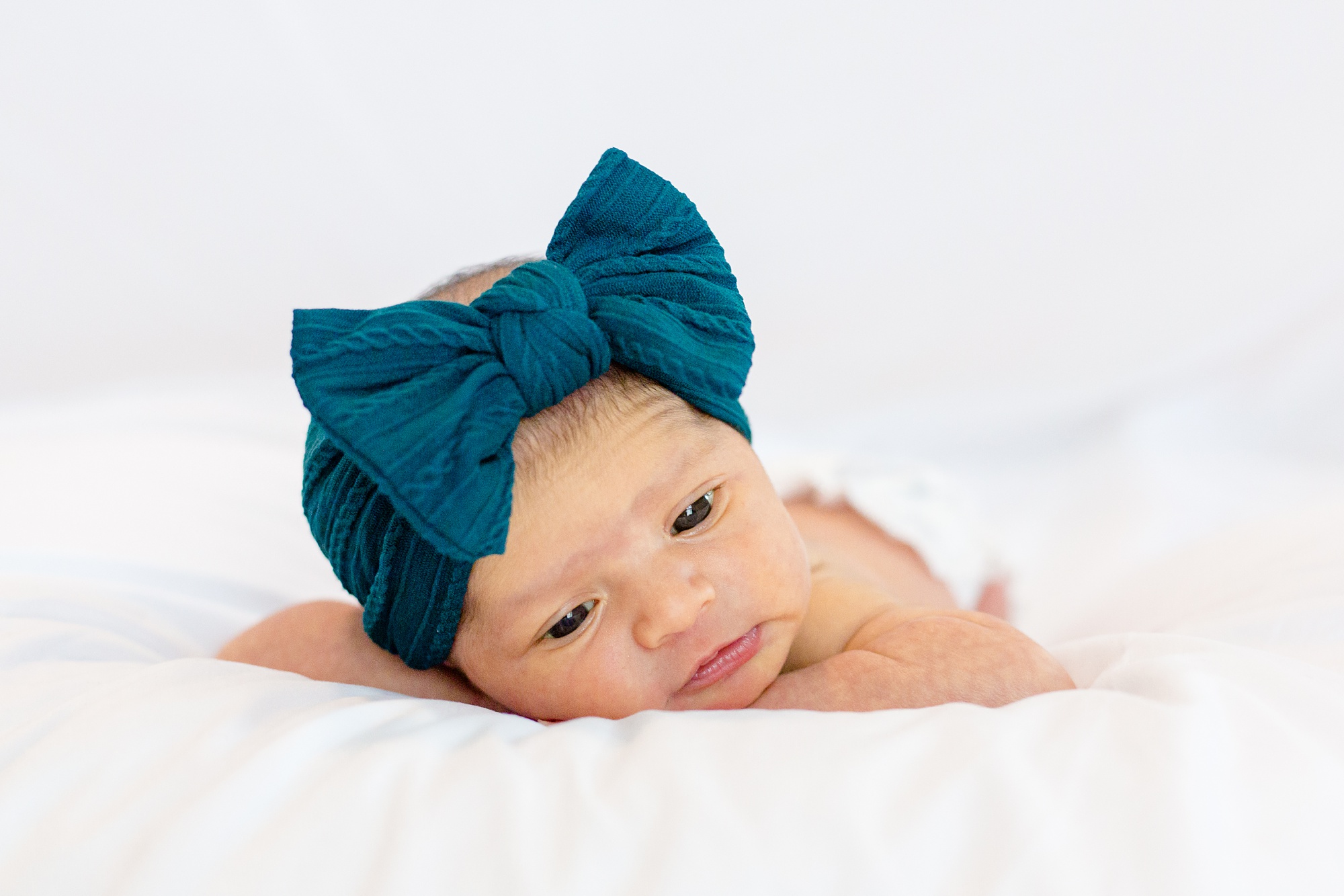 baby girl lays on bed with teal bow