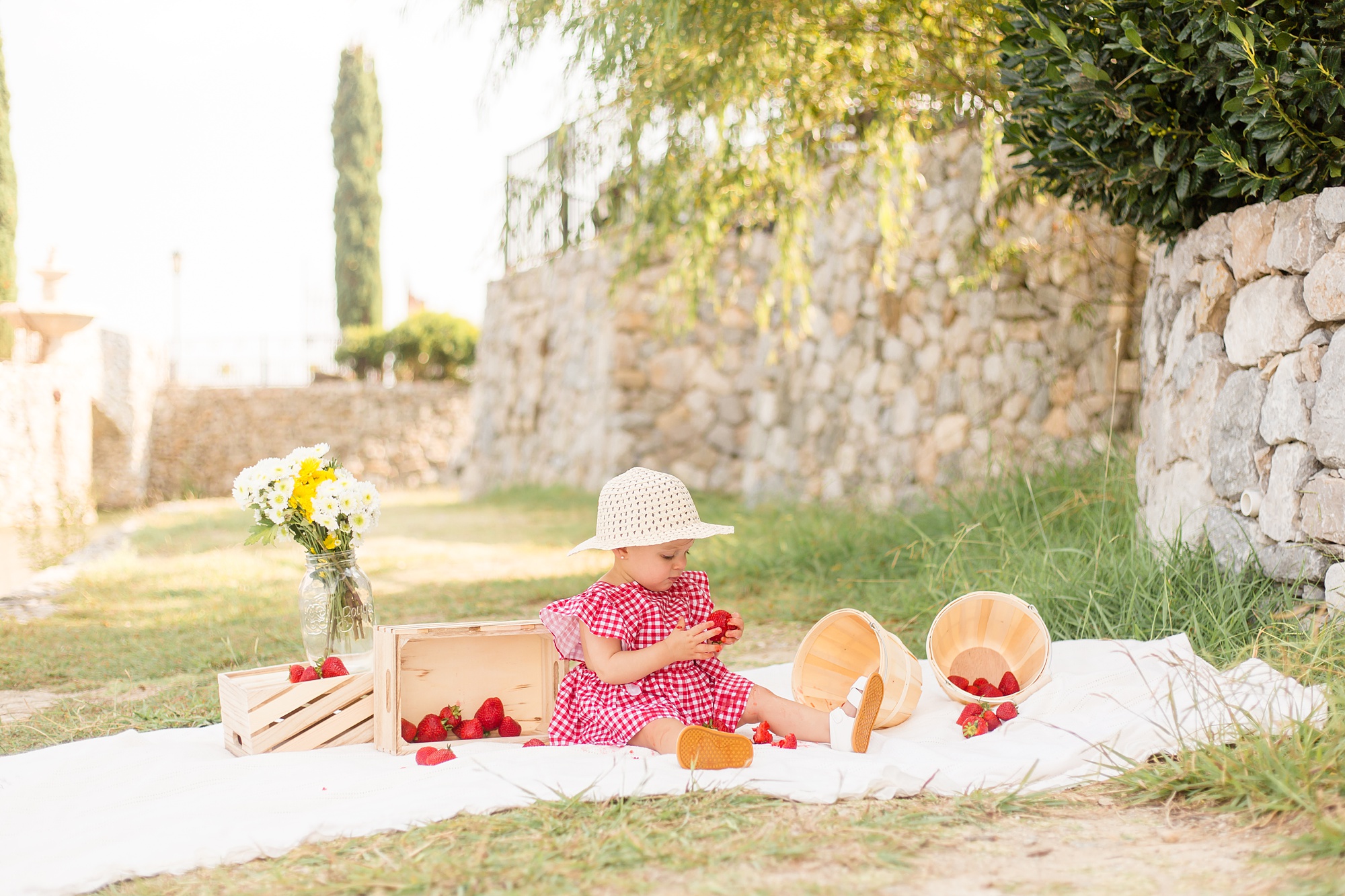 toddler in hat plays with strawberries for first birthday session