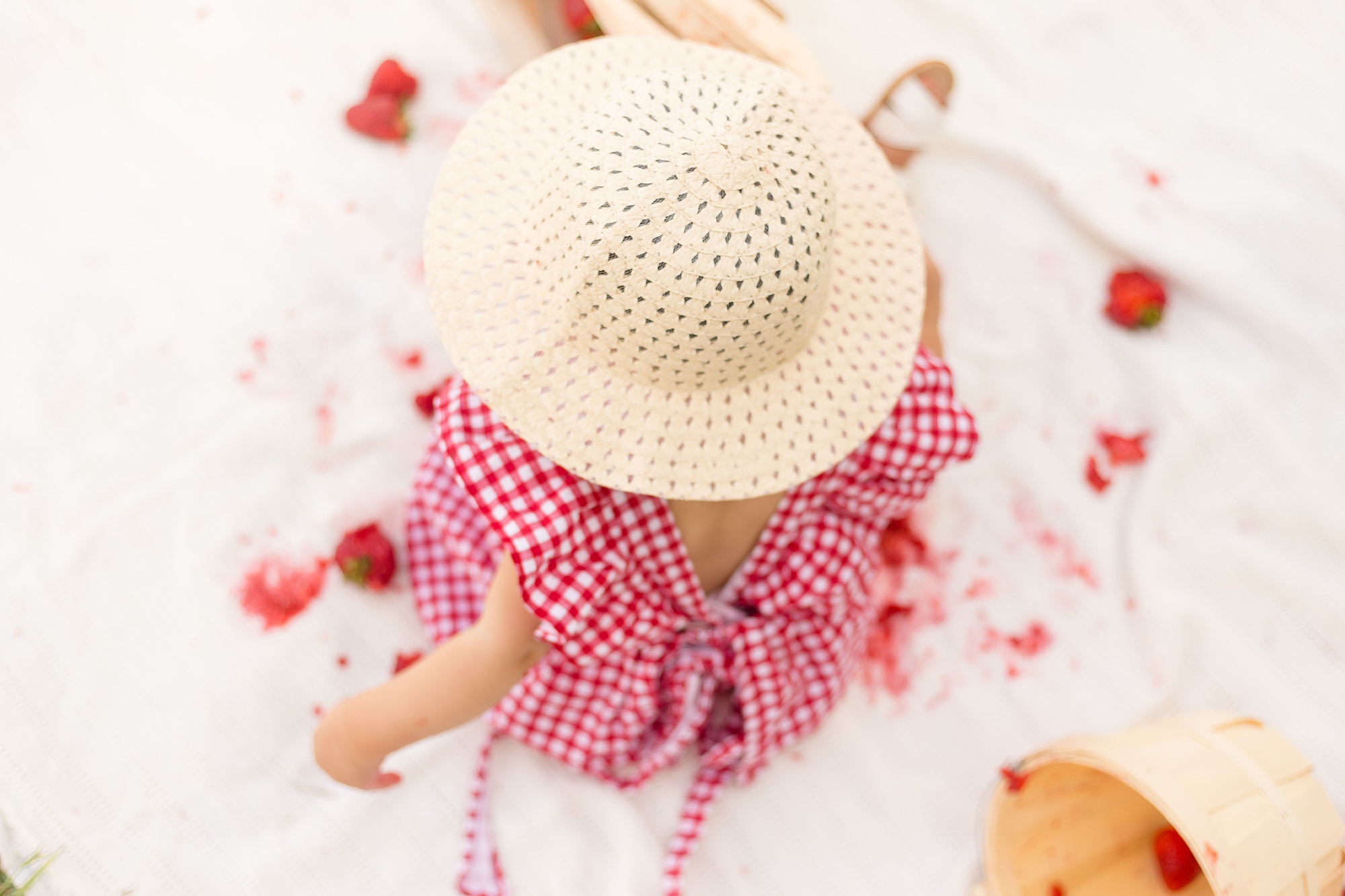 baby in straw hat plays with strawberries