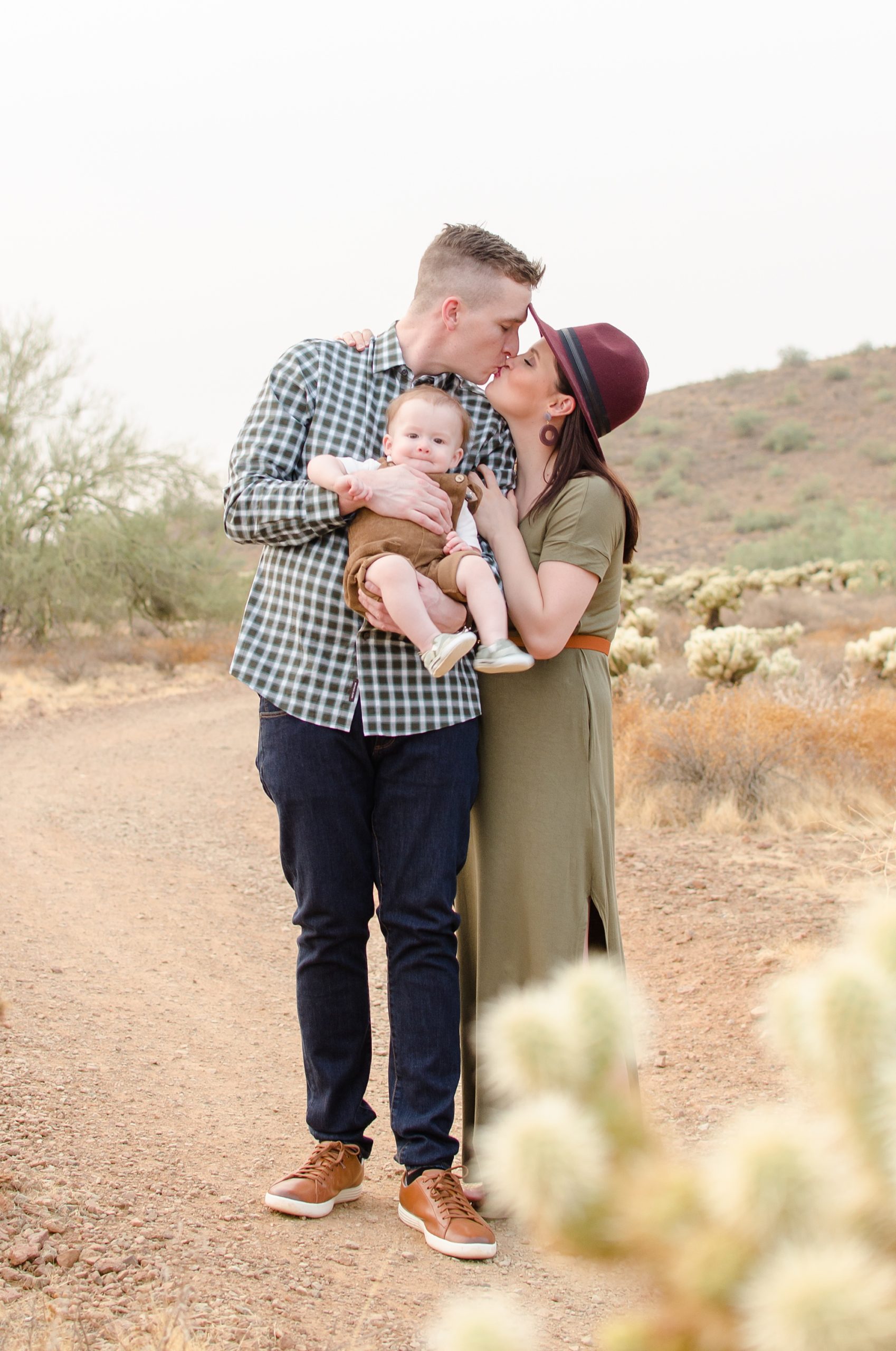 couple kisses while holding son during Apache Wash Trailhead family photos