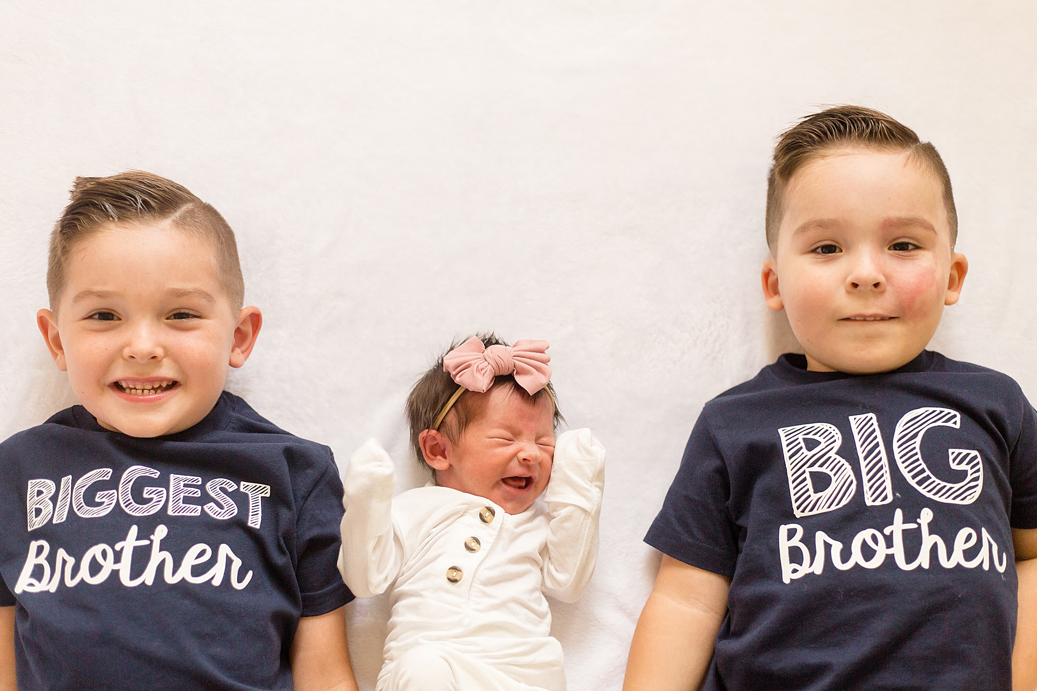baby sister cries laying between two brothers during At Home Lifestyle Newborn Session