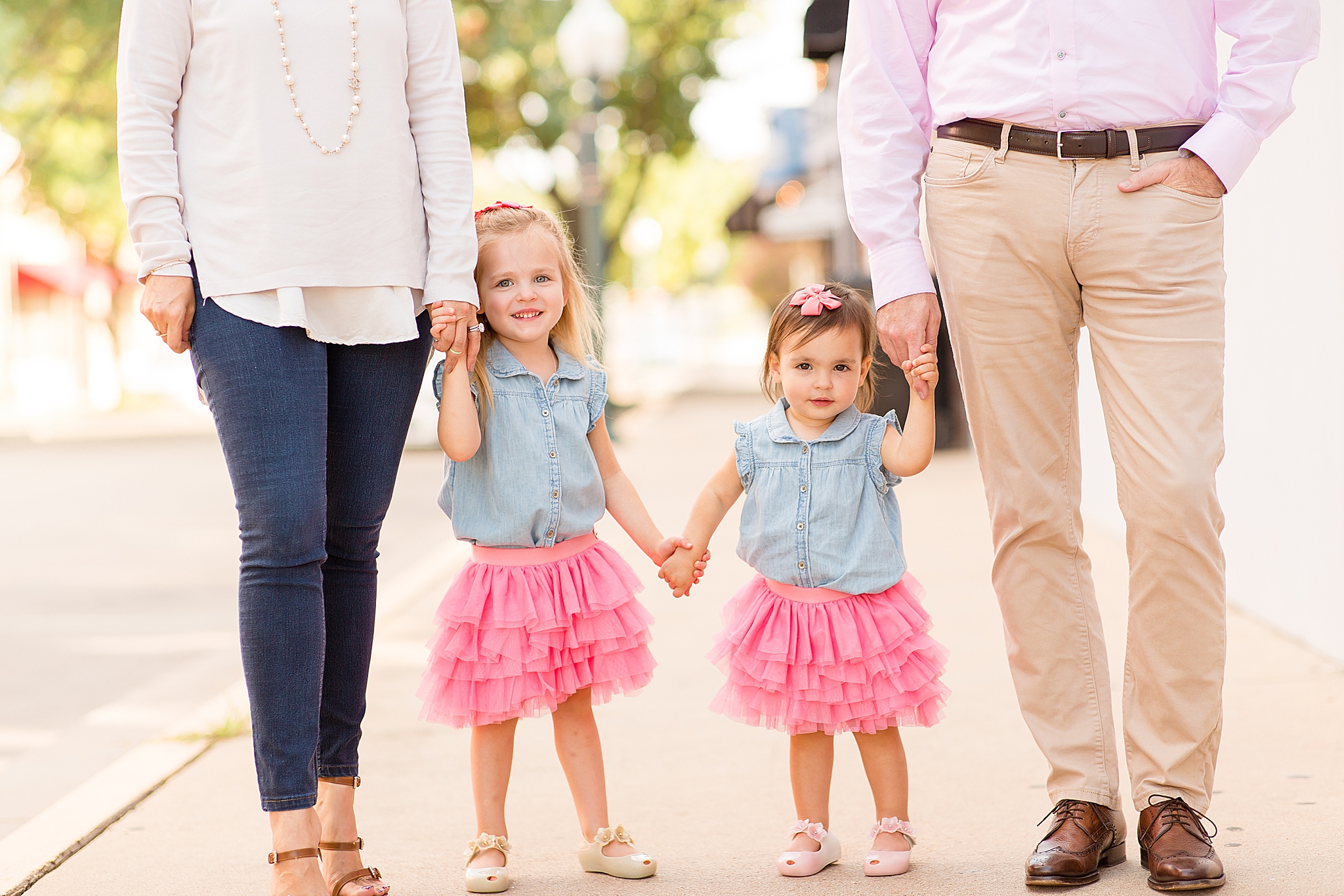 sisters in matching pink and blue outfits hold parents' hands