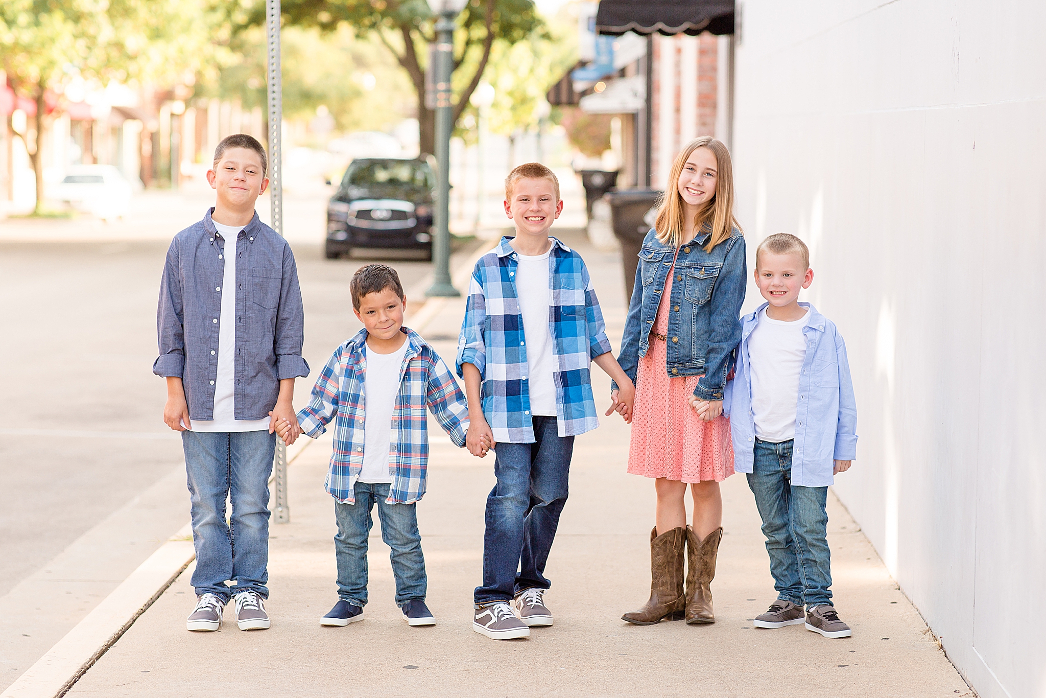 five siblings stand holding hands on sidewalk