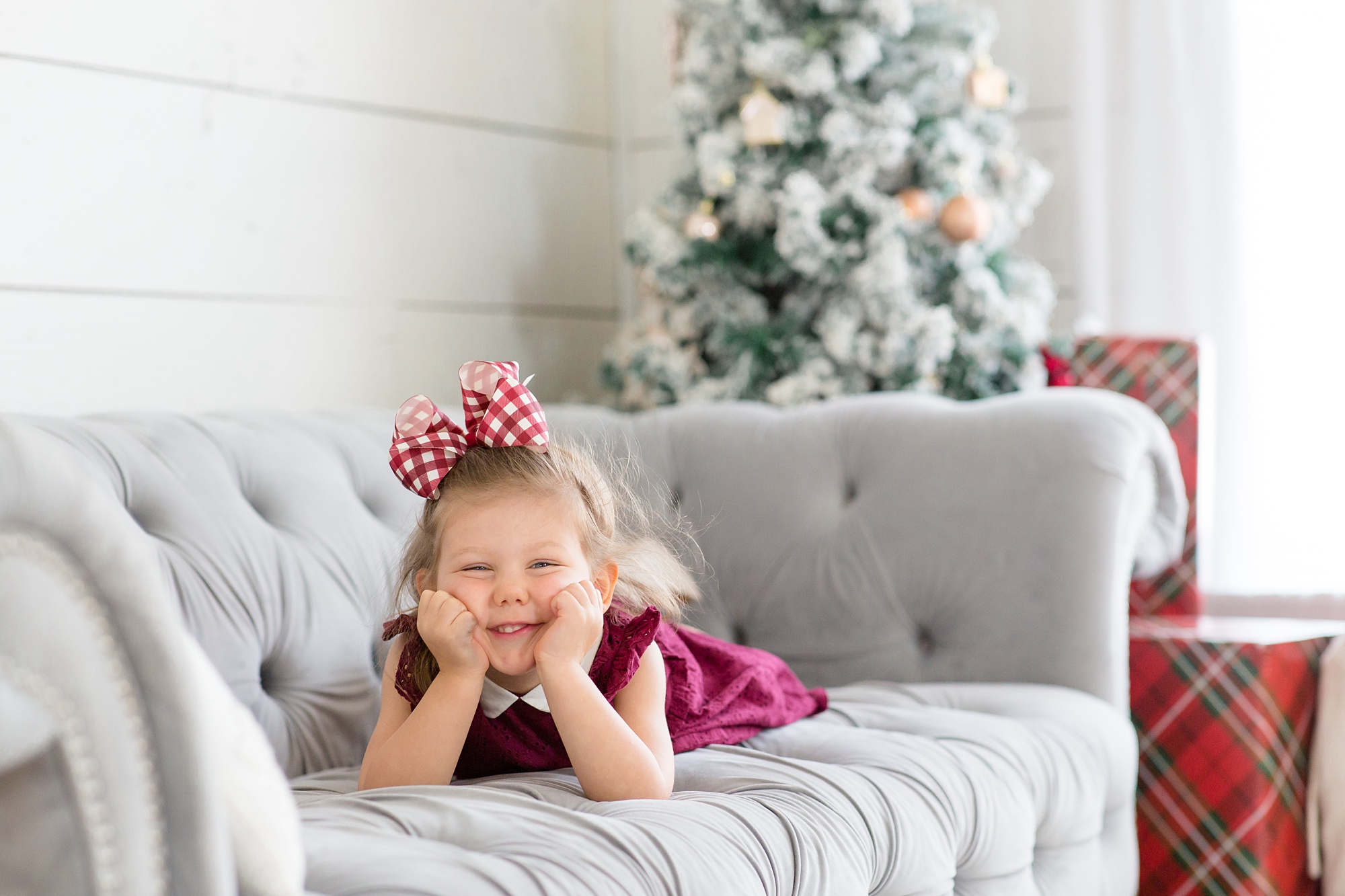 little girl lays on grey couch with Christmas tree behind her