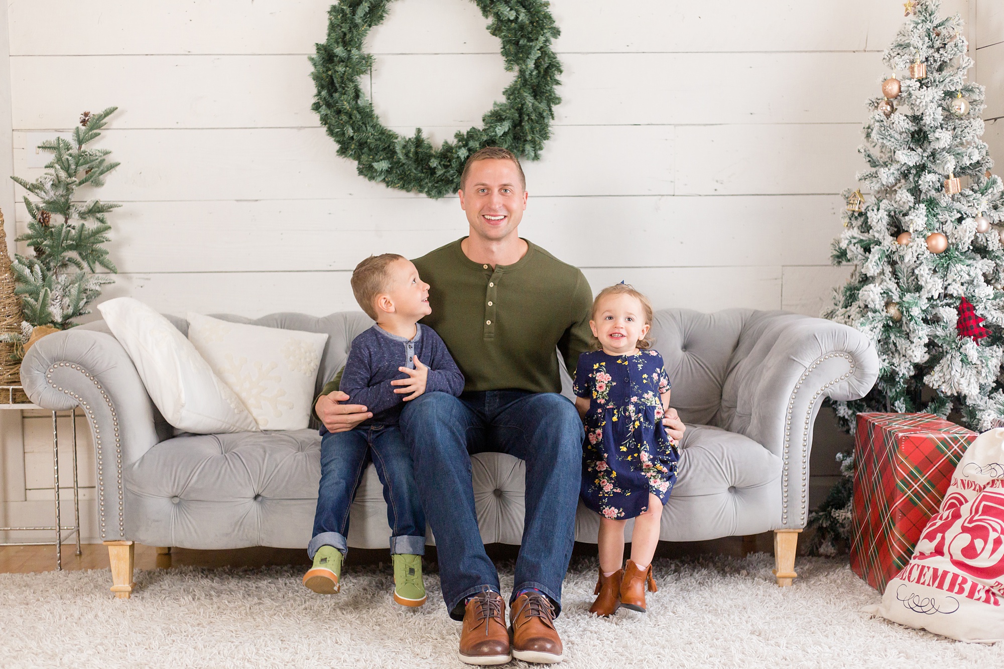 boys sit with dad on grey couch in front of holiday wreath