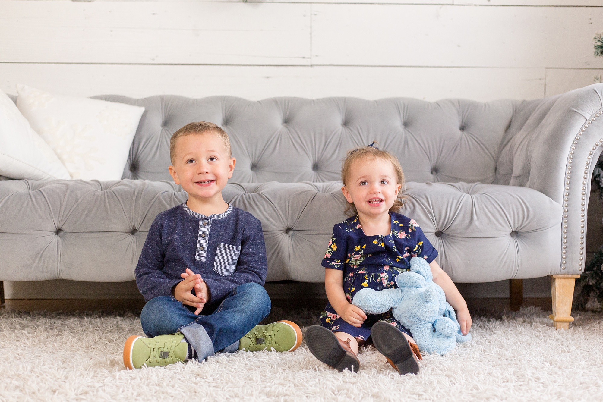 siblings sit in front of grey couch