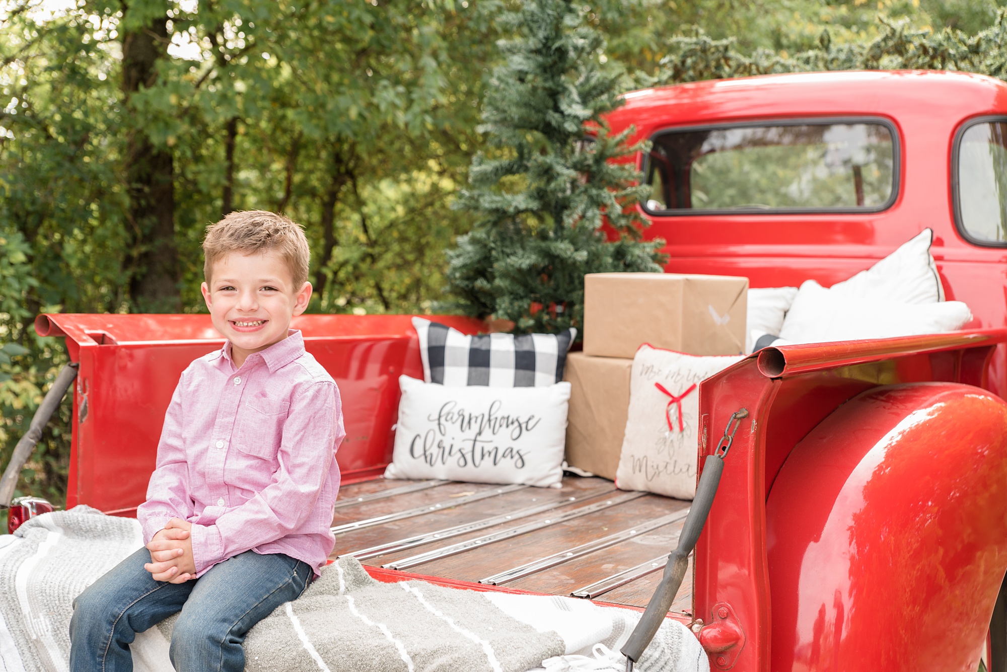 young boy sits on bed of truck with Christmas presents behind him