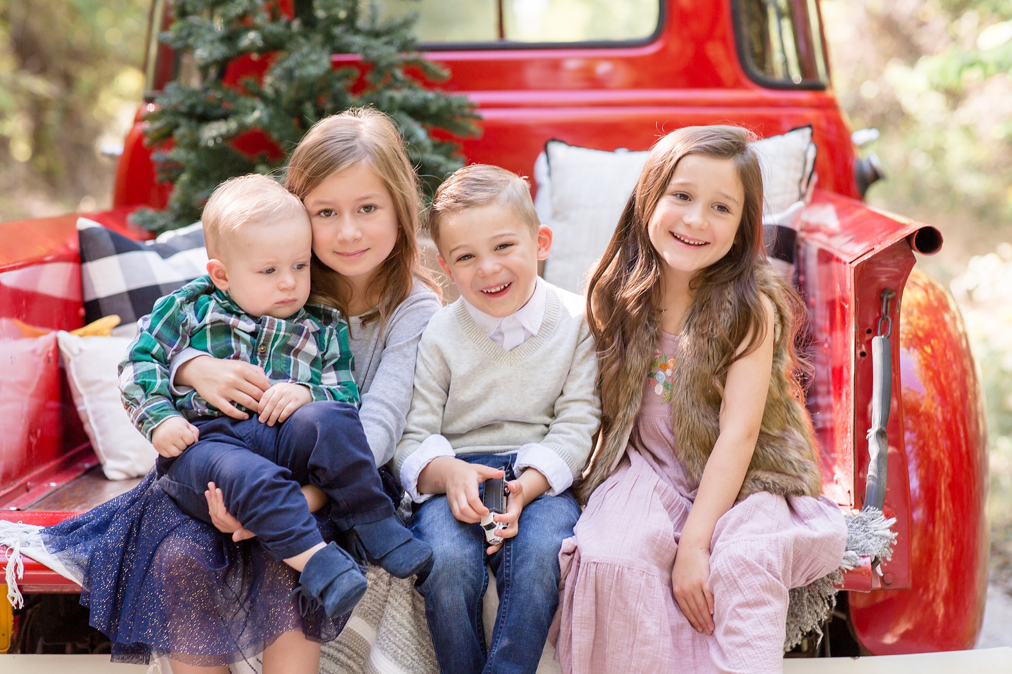 four siblings sit on truck during Texas Red Truck Christmas minis