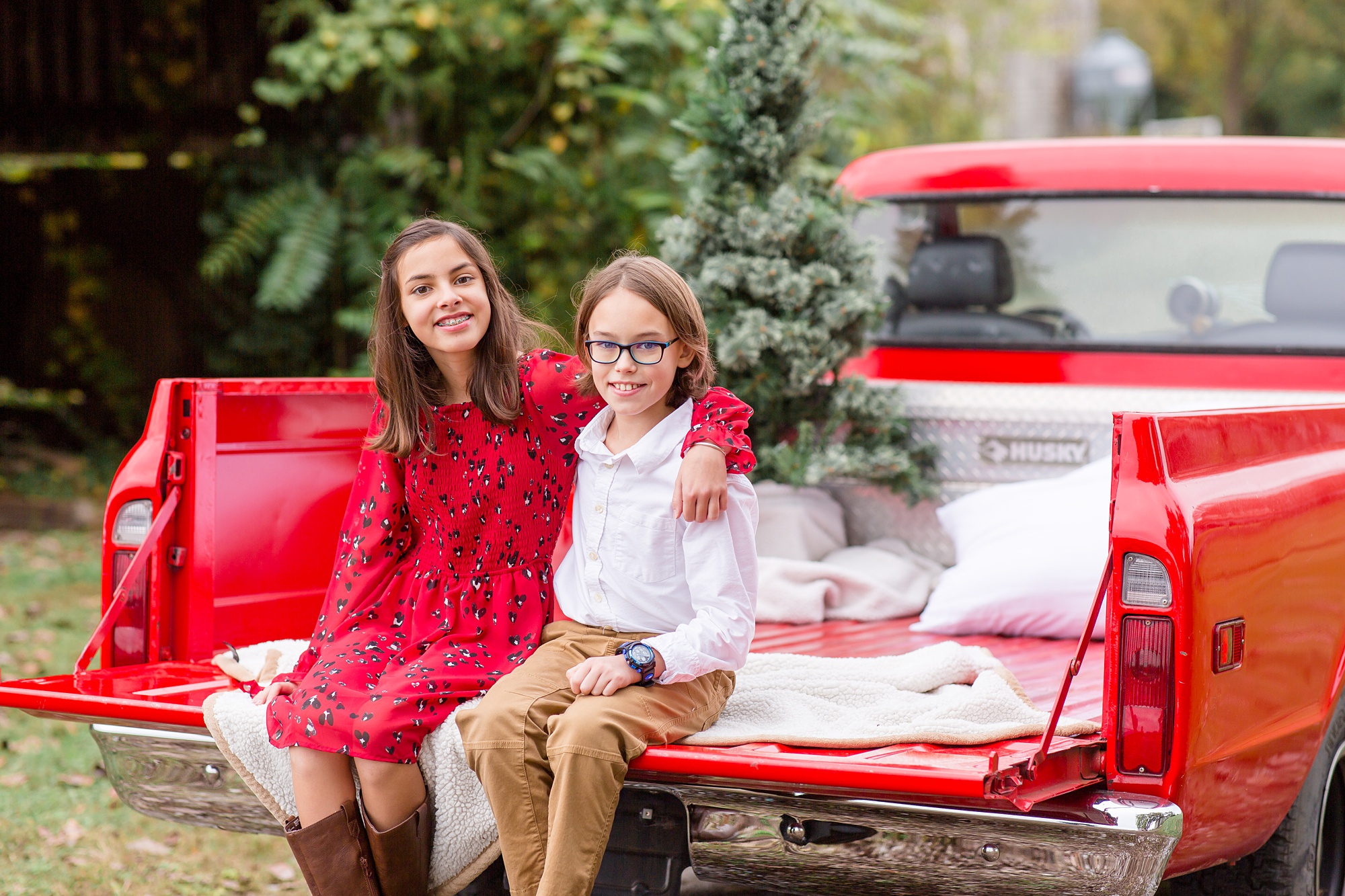 siblings pose in the back of red truck during holiday mini sessions