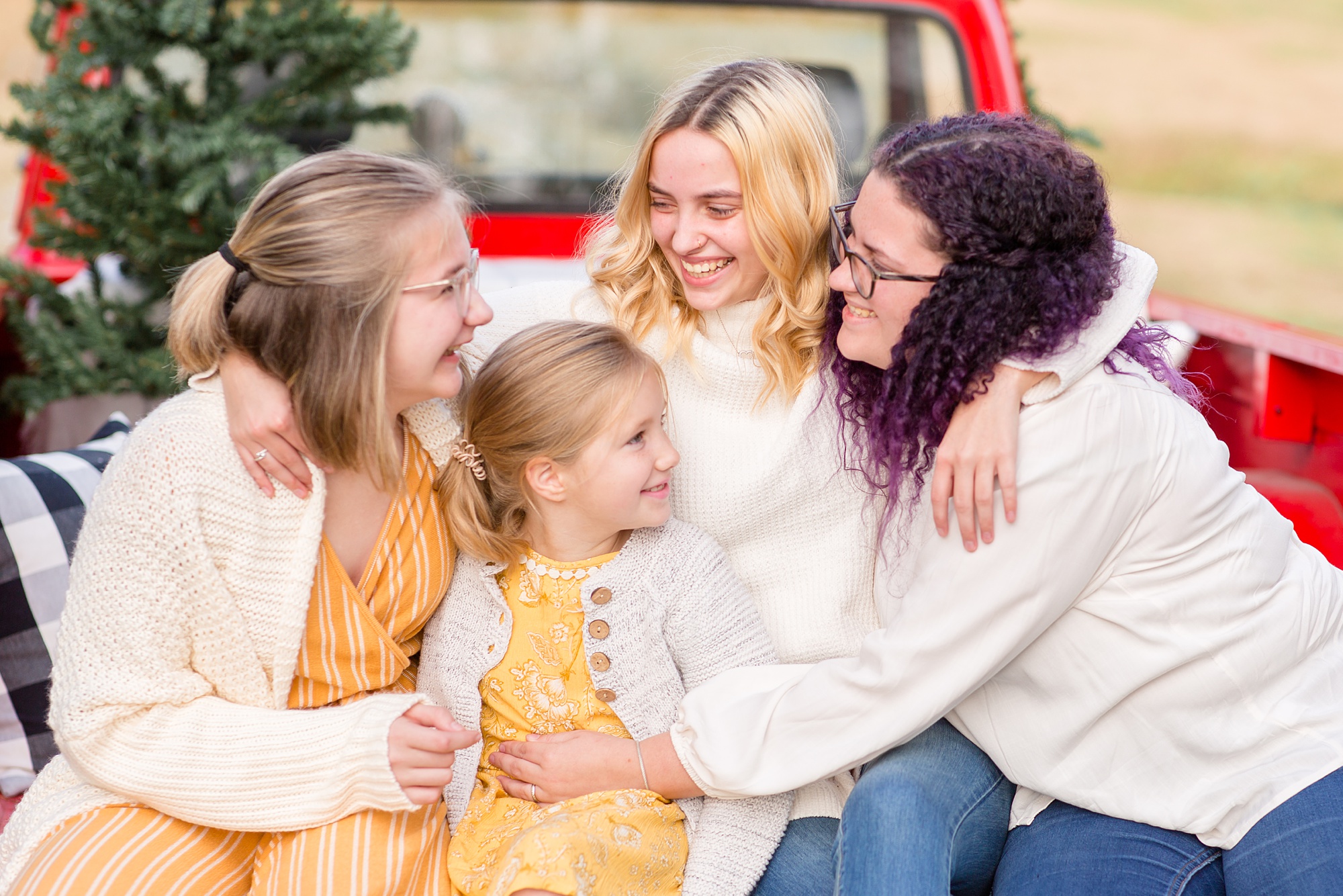 four sisters hug in back of red truck during Tennessee Red Truck Christmas Minis