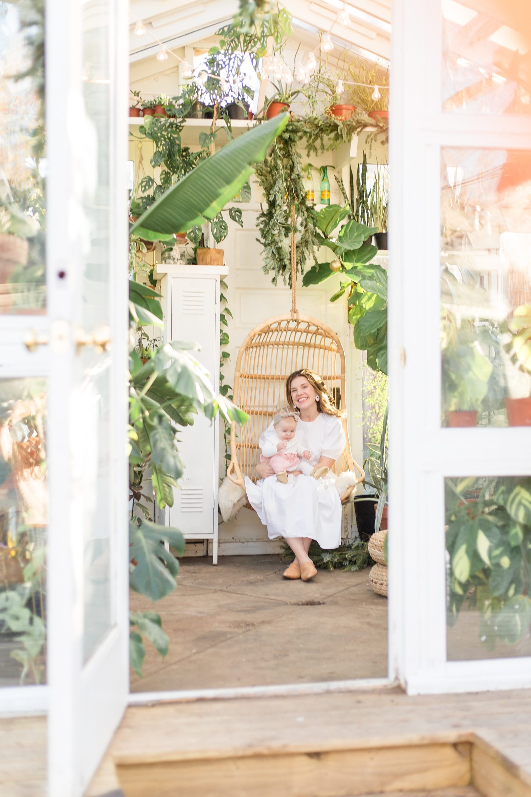 mom sits on chair with two girls during family photos in greenhouse