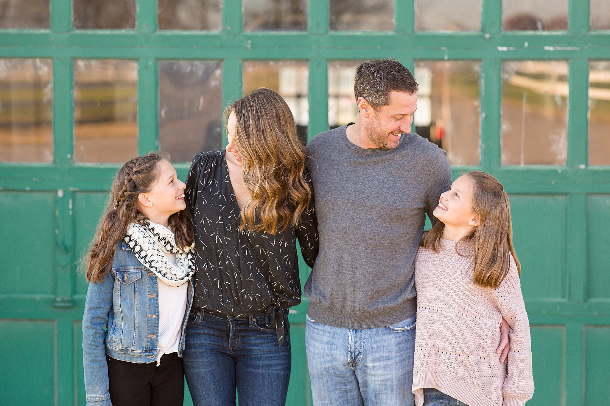family of four poses in front of green barn door