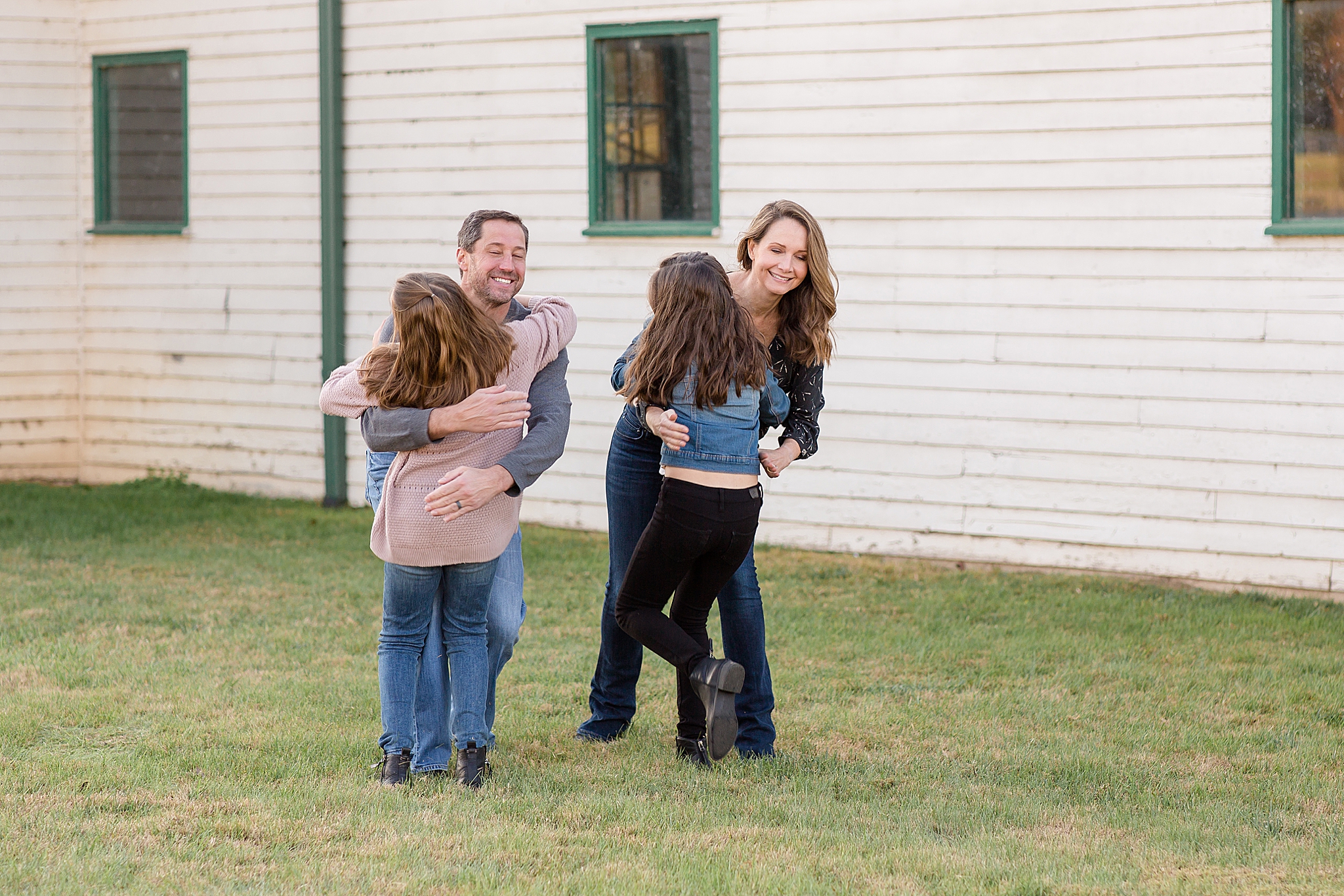 daughters hug parents by white barn