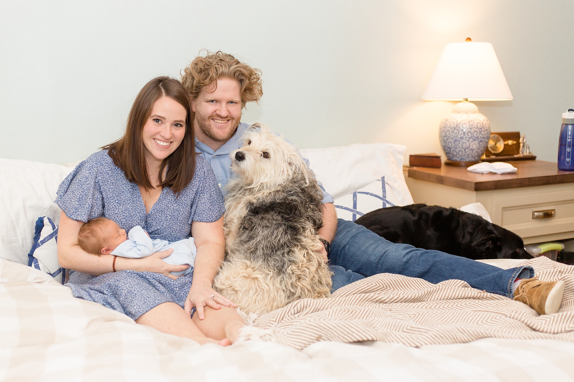 parents sit on bed with new baby boy and dog in Nashville TN home