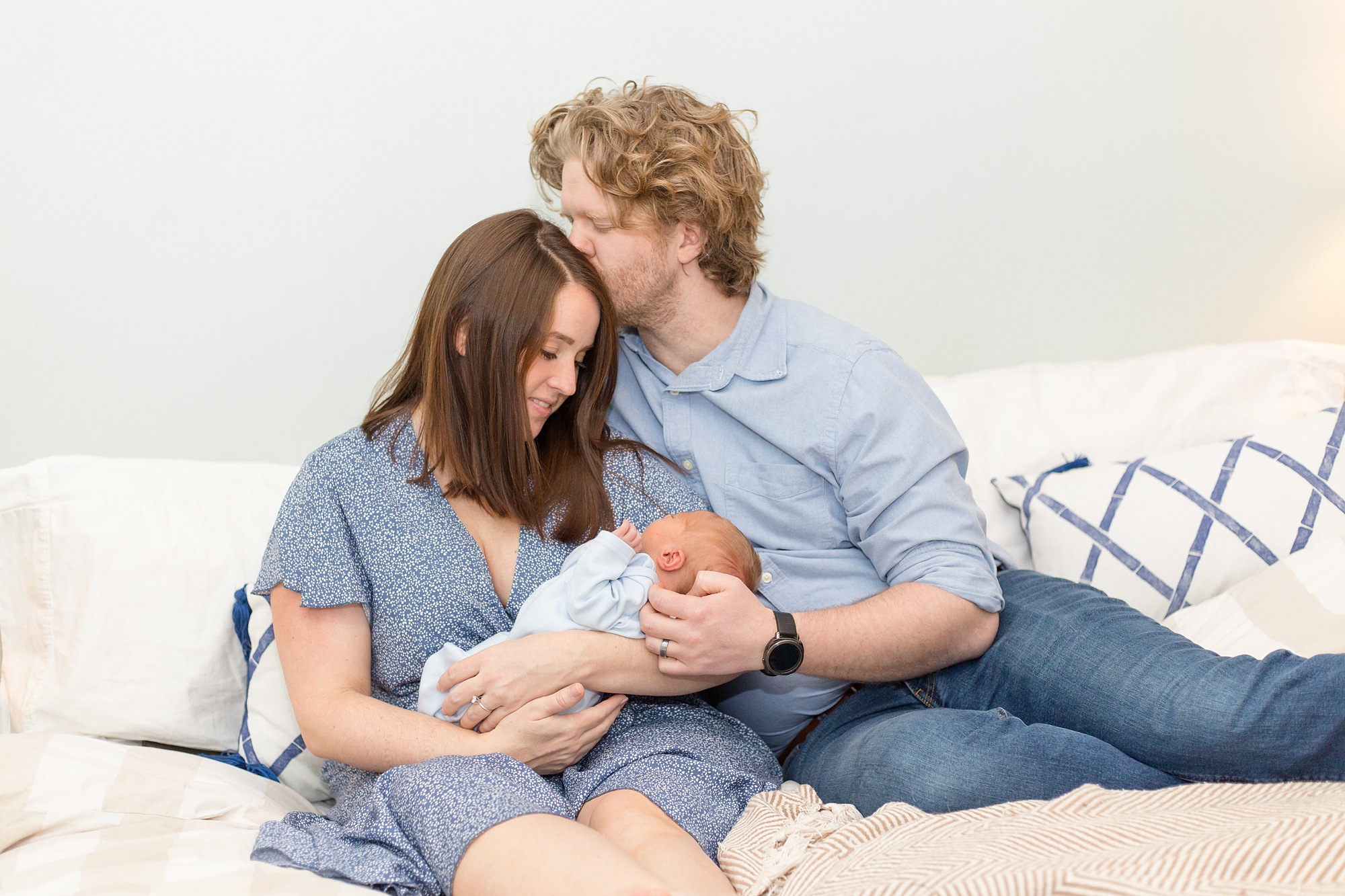 husband kisses wife's forehand while cuddling baby boy