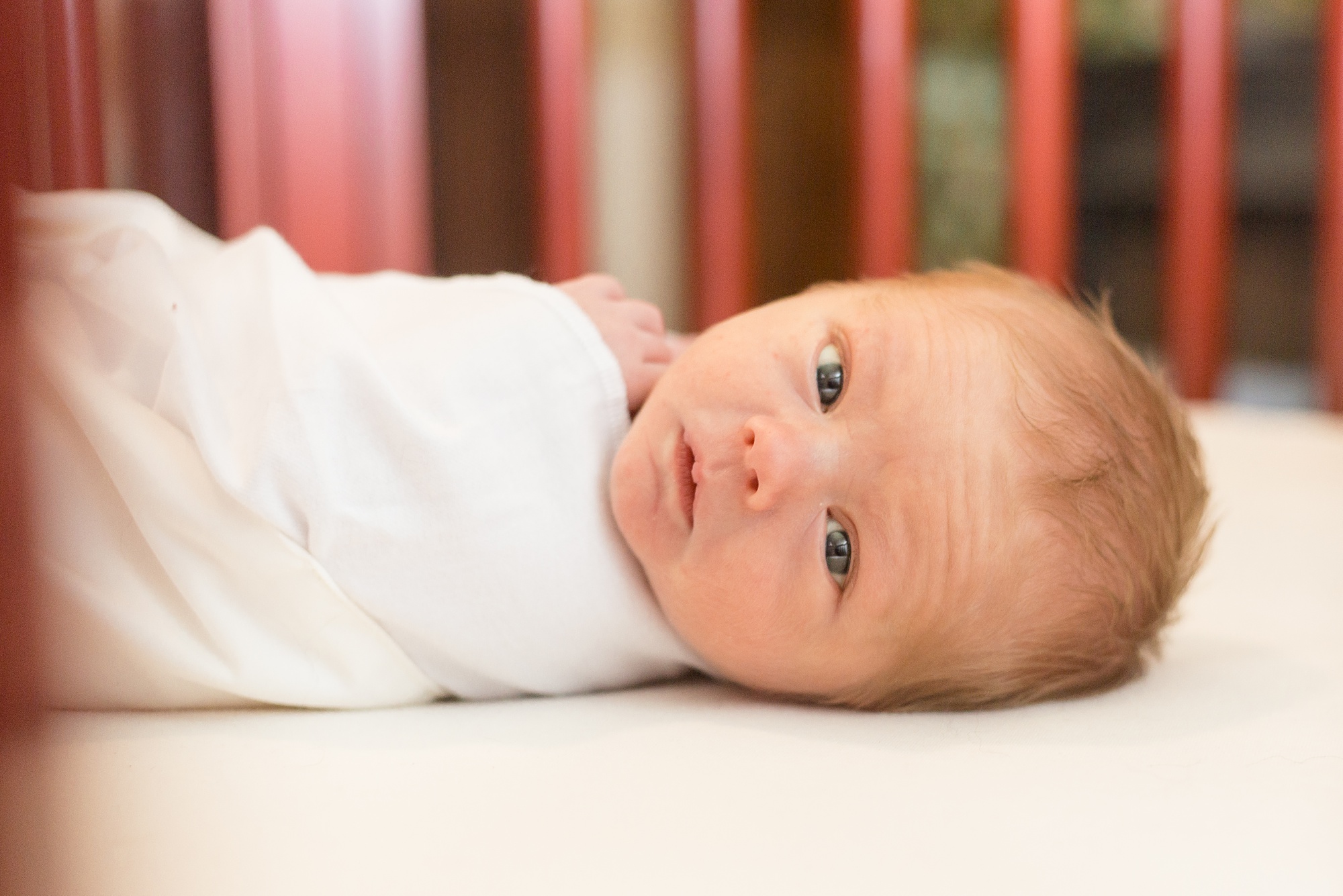 baby boy looks through rails in crib during newborn photos
