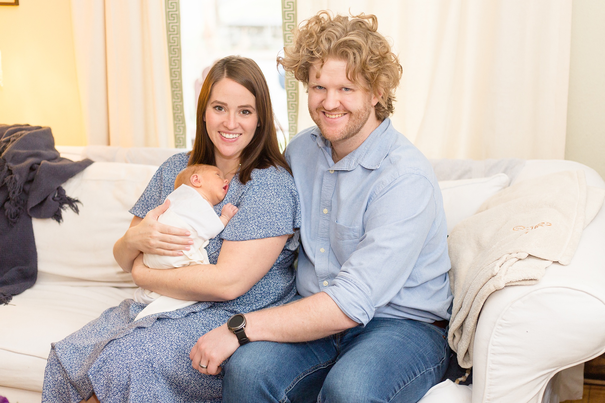 parents sit on couch with new baby at home