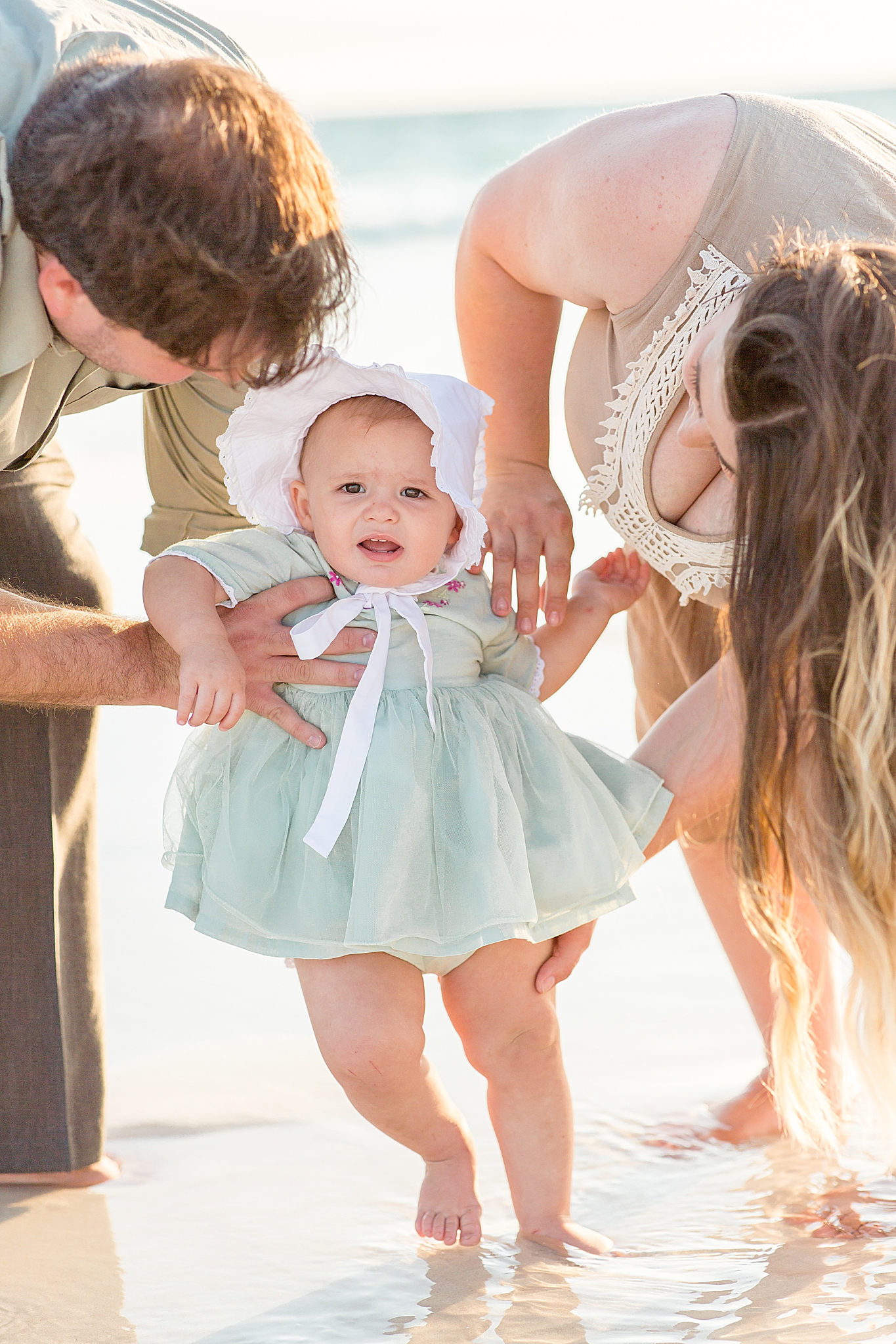 parents help baby girl stand up in light blue dress
