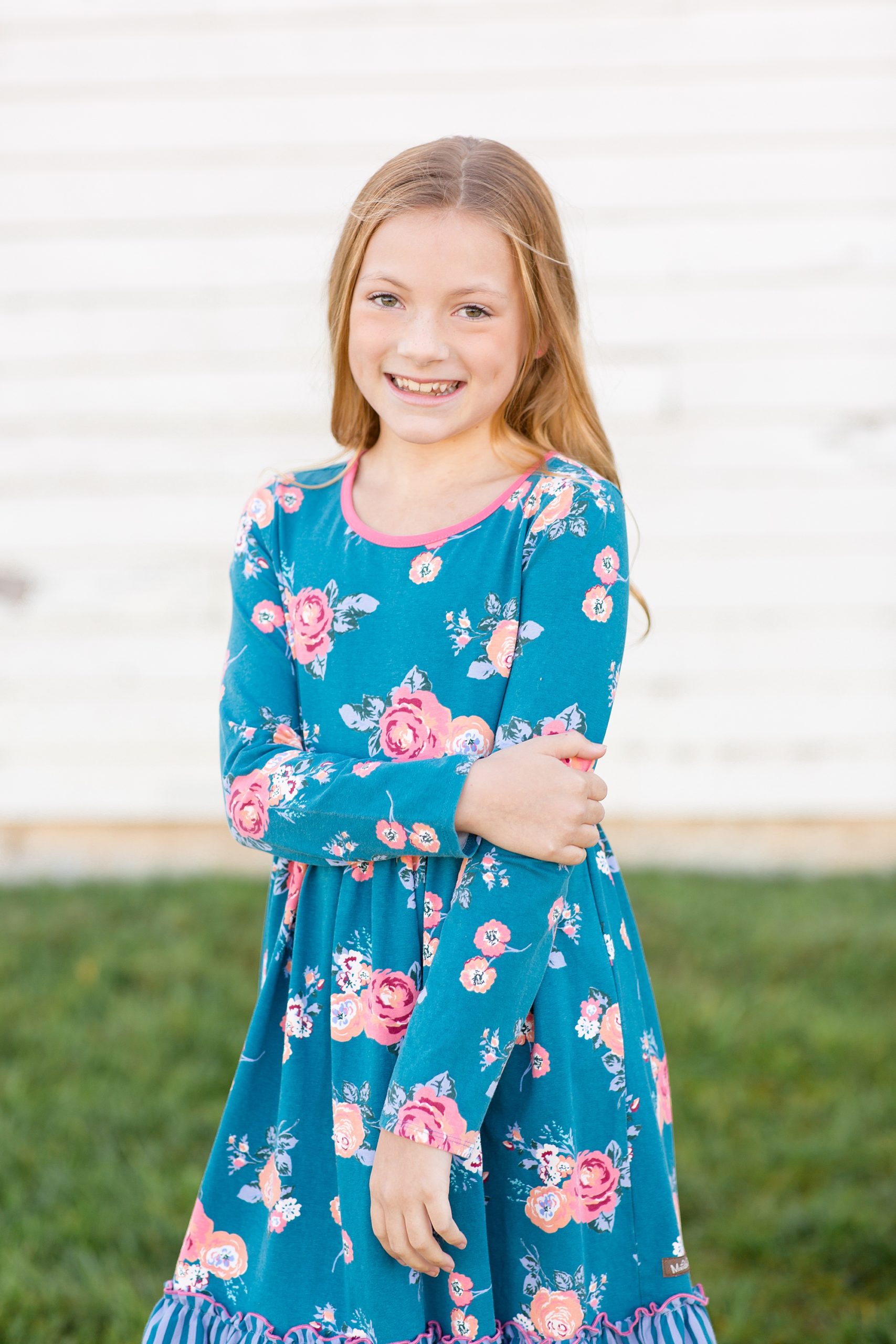 daughter in floral dress poses by white barn