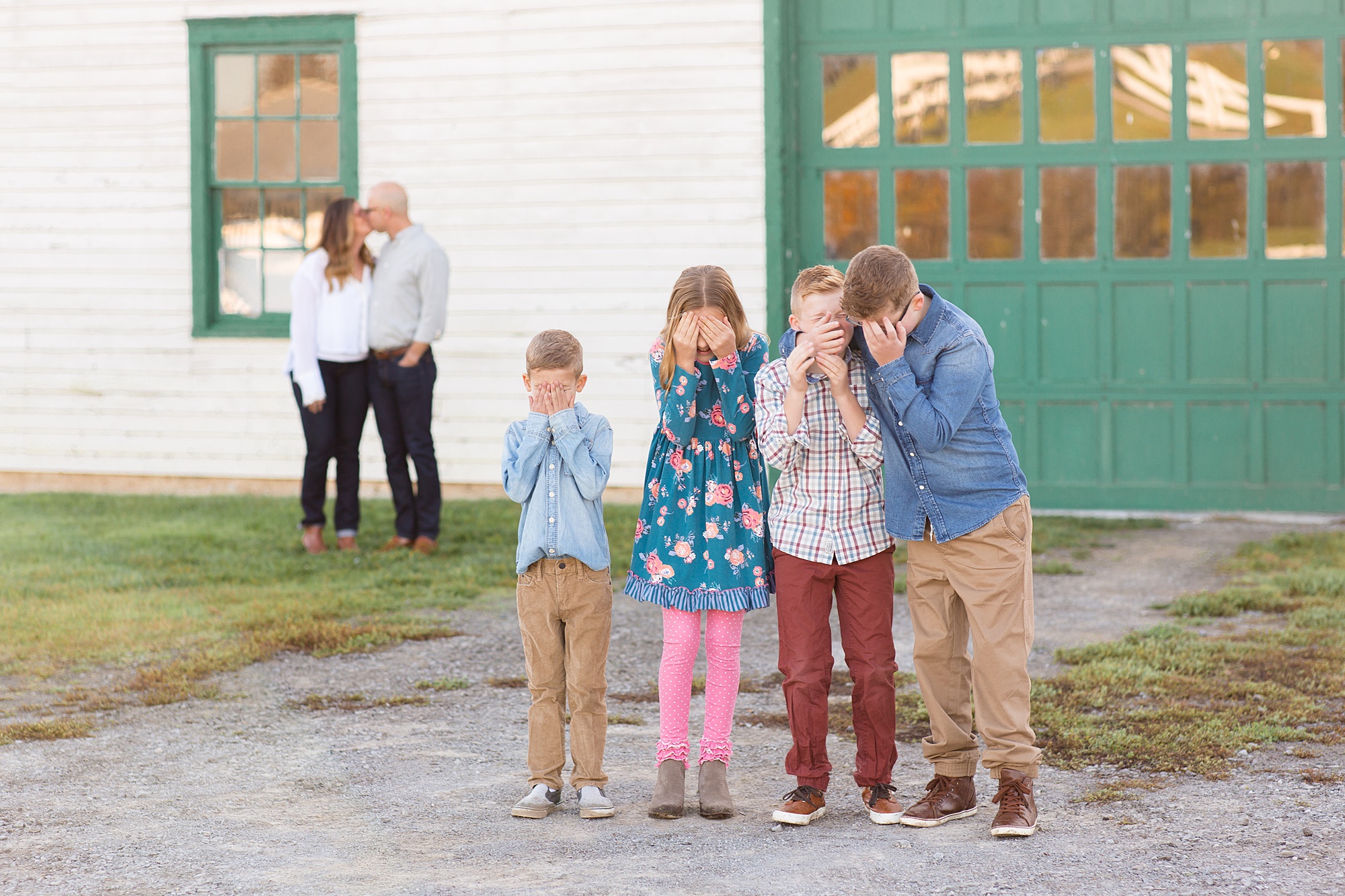 kids cover eyes while parents kiss by white barn