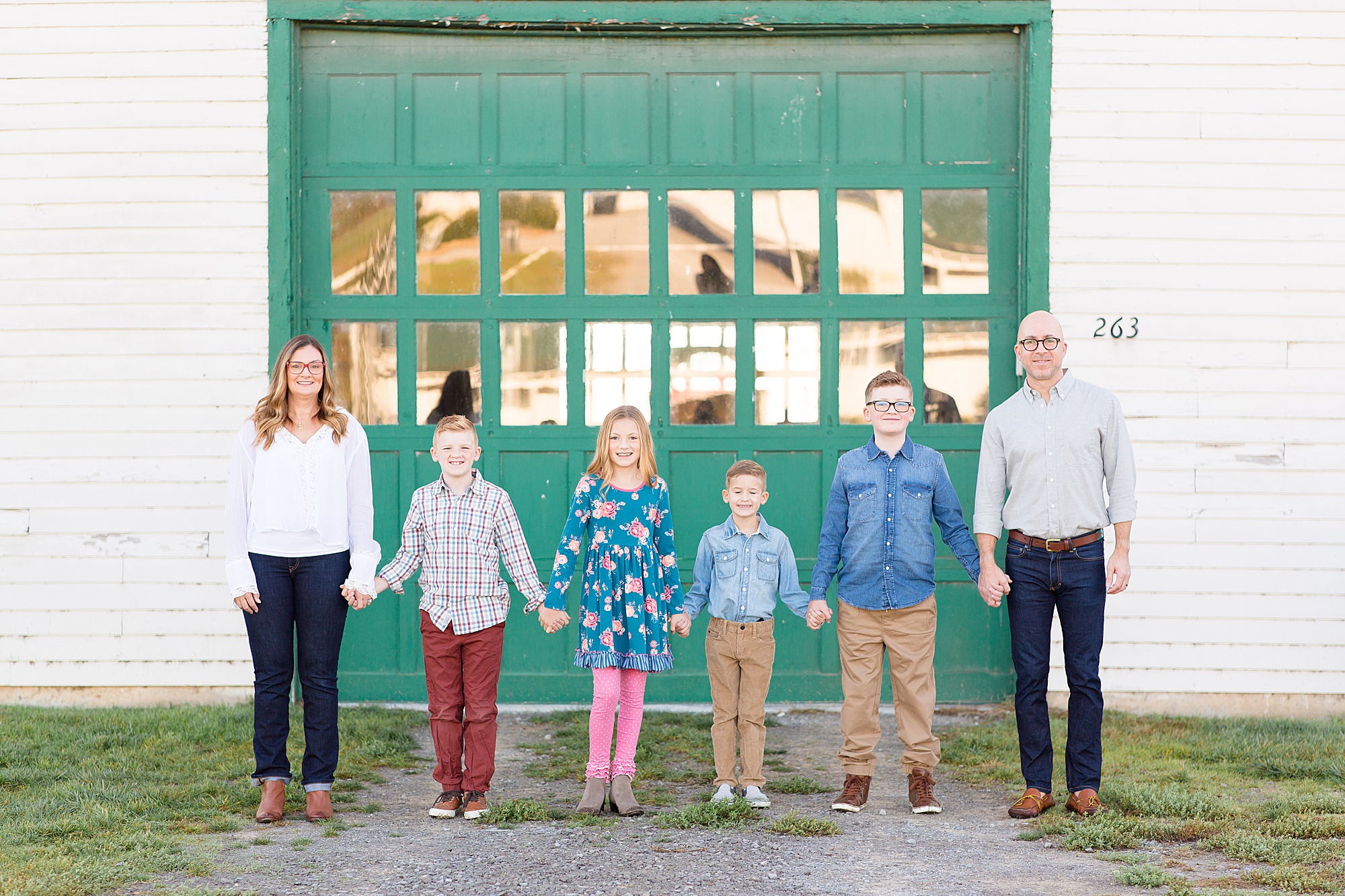 family of six holds Hands standing by green barn door