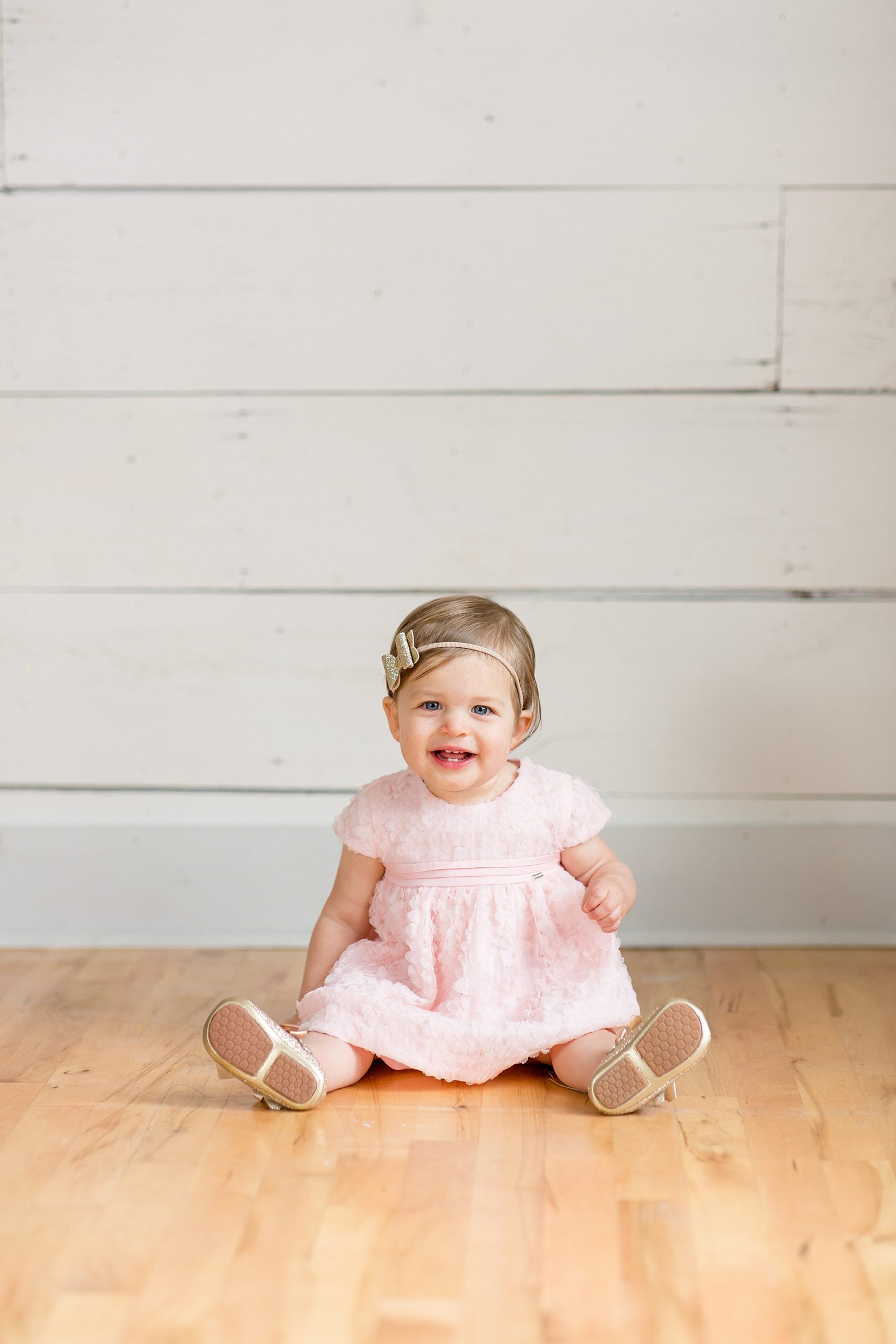 baby girl in pink dress sits on wood floor during cake smash