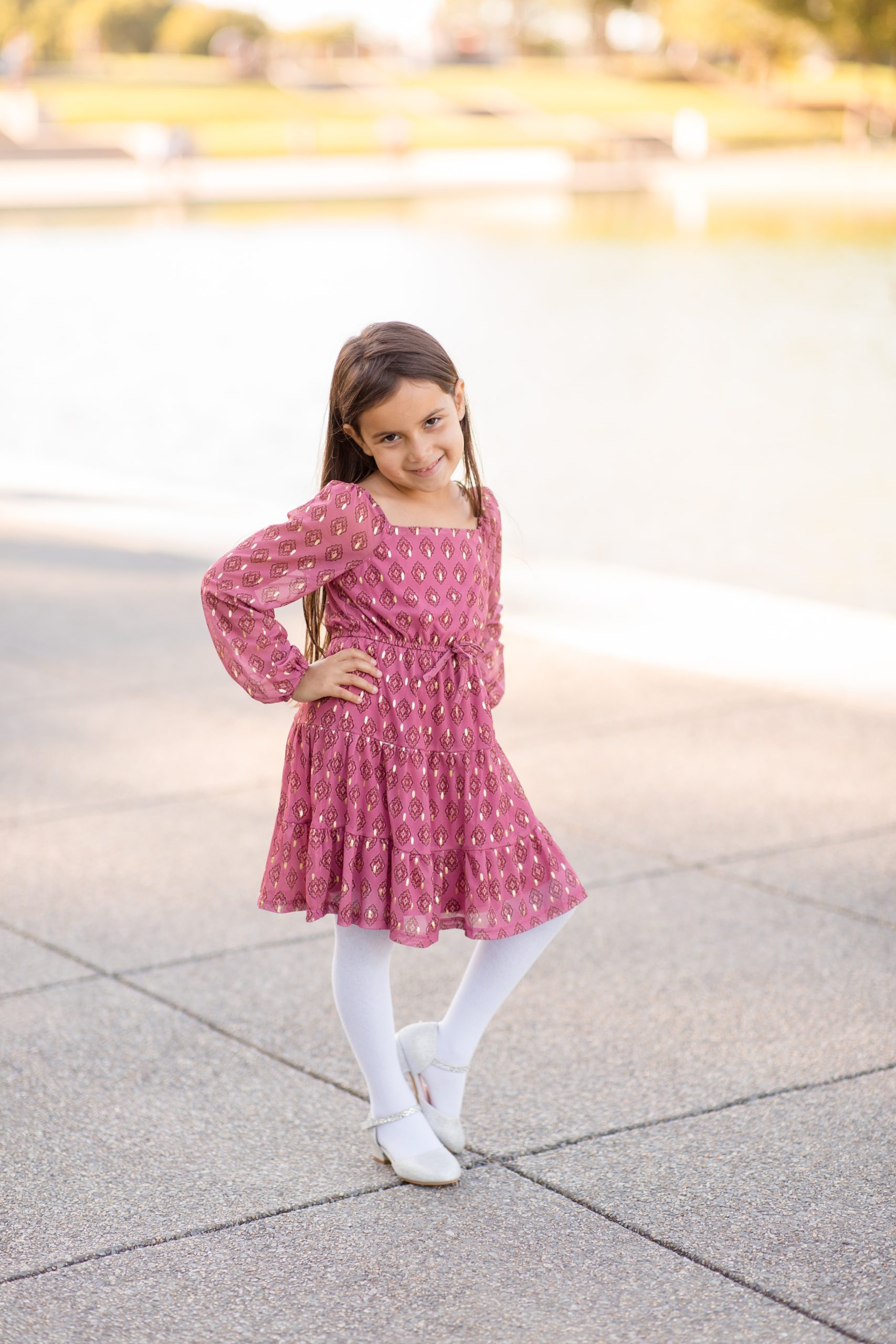 Young girl in pink dress and tights poses in front of War Memorial in Washington, DC during family portrait session with Rebecca Rice Photography