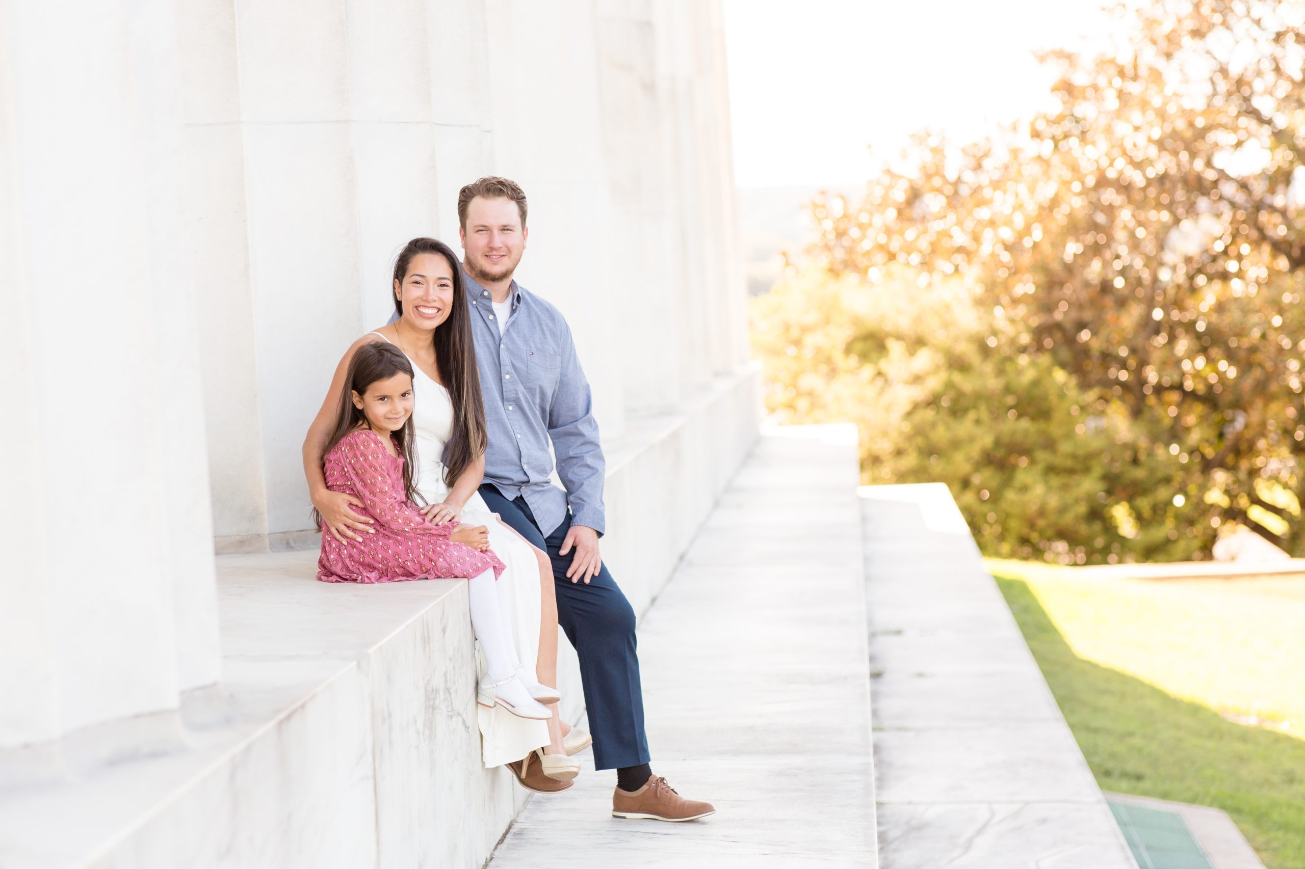 family of 3 sits on stairs of memorial in Washington DC for family portrait session with Rebecca Rice Photography