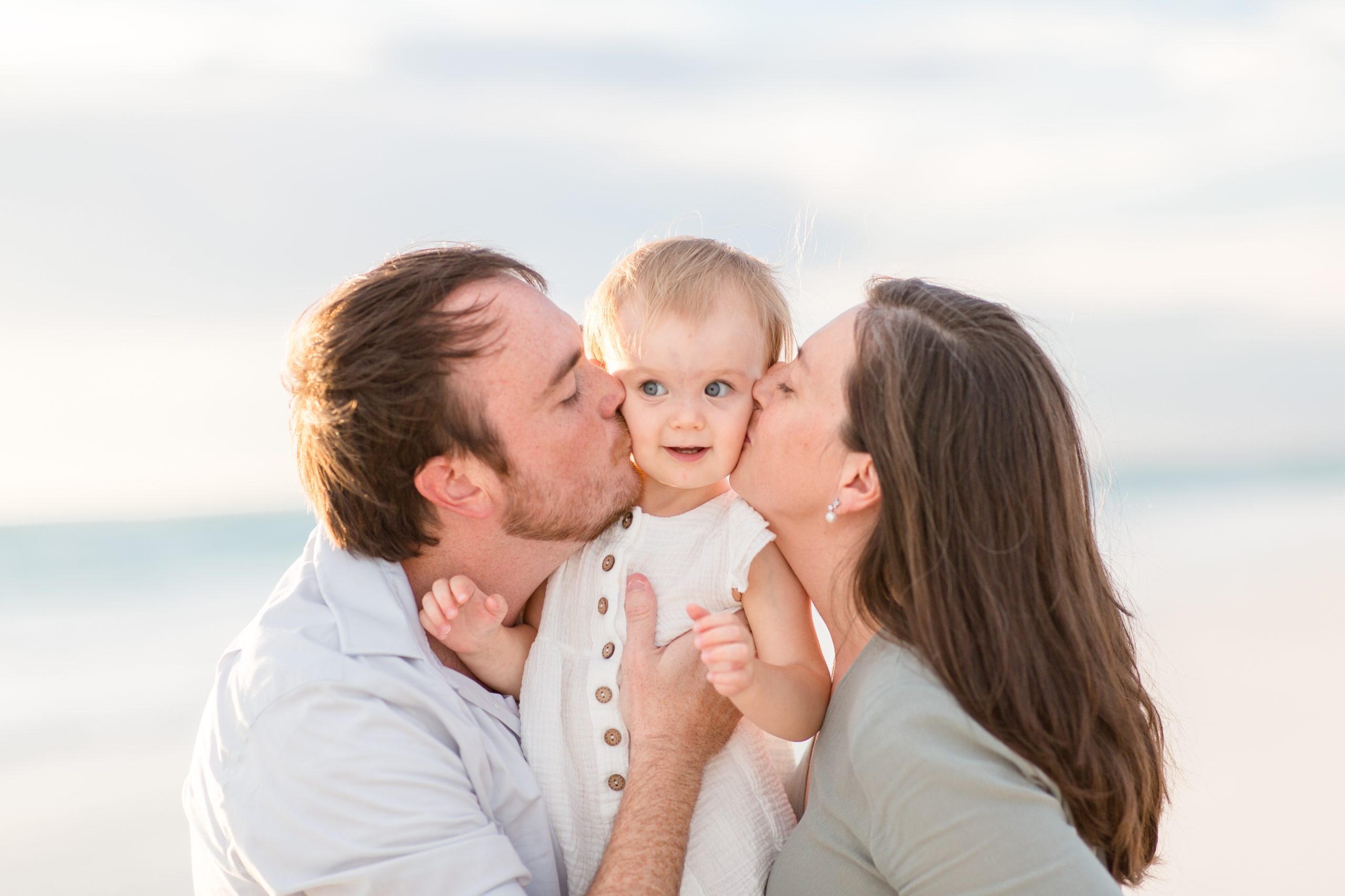 Mom and dad kiss baby girl during family portrait session on Anna Maria Island in Florida with family photographer Rebecca Rice Photography. Click to read more about this sweet session on the blog now!