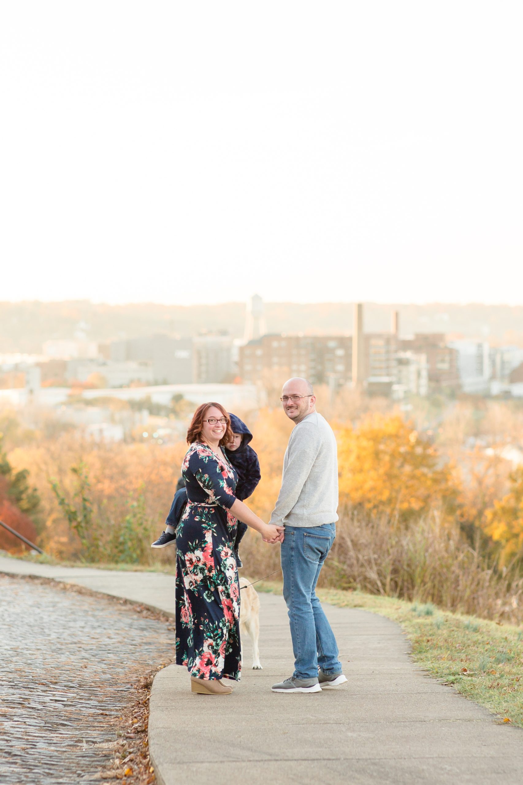 Family of 3 walks on sidewalk at Libby Hill Park overlooking Richmond, VA during family portrait session with family photographer Rebecca Rice Photography. Click to read more about this sweet family session on the blog now!