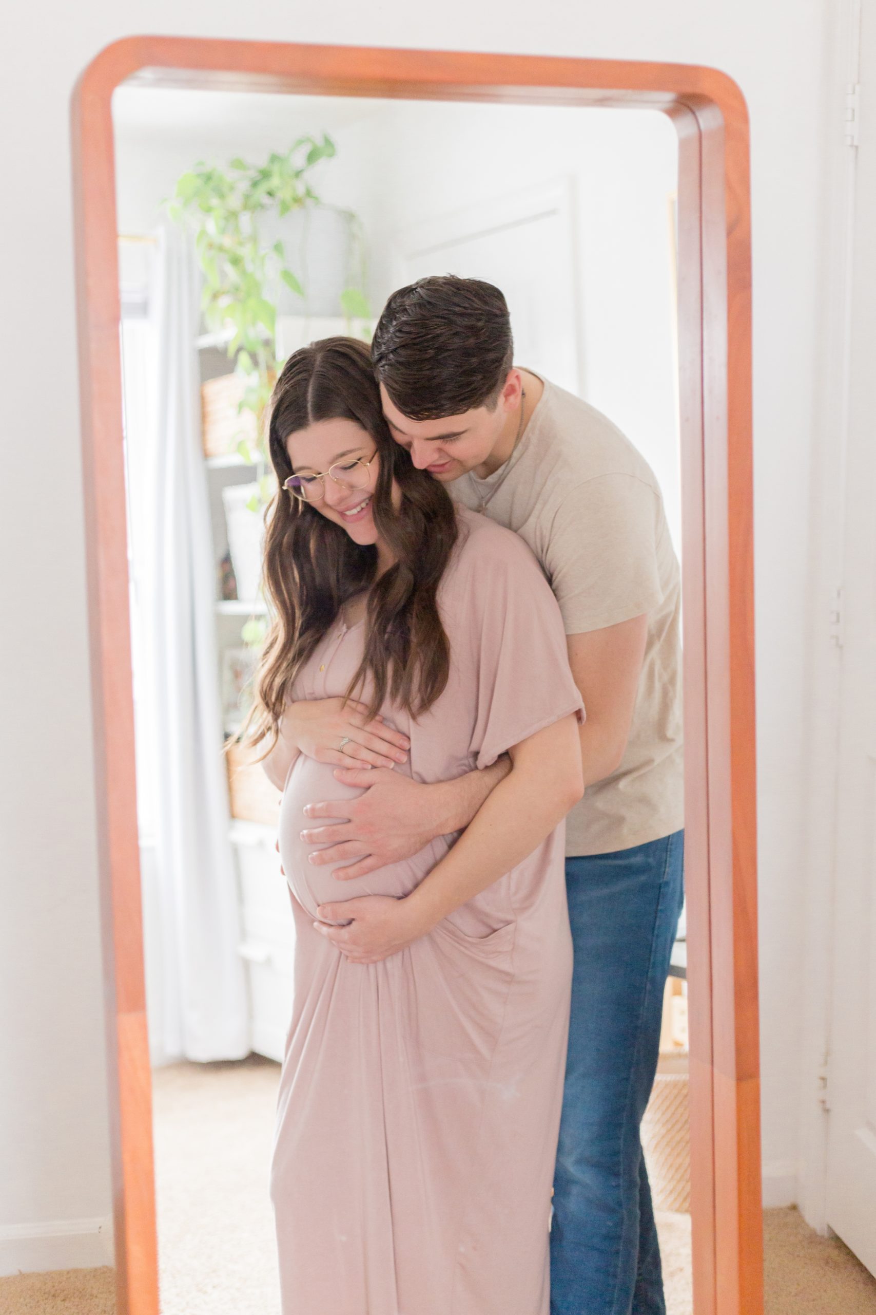 Expecting parents hold pregnant belly of mom in pink dress in front of mirror in home during maternity photo session with Rebecca Rice of Rebecca Rice Photography. Click to see more from this precious session live on the blog now! 