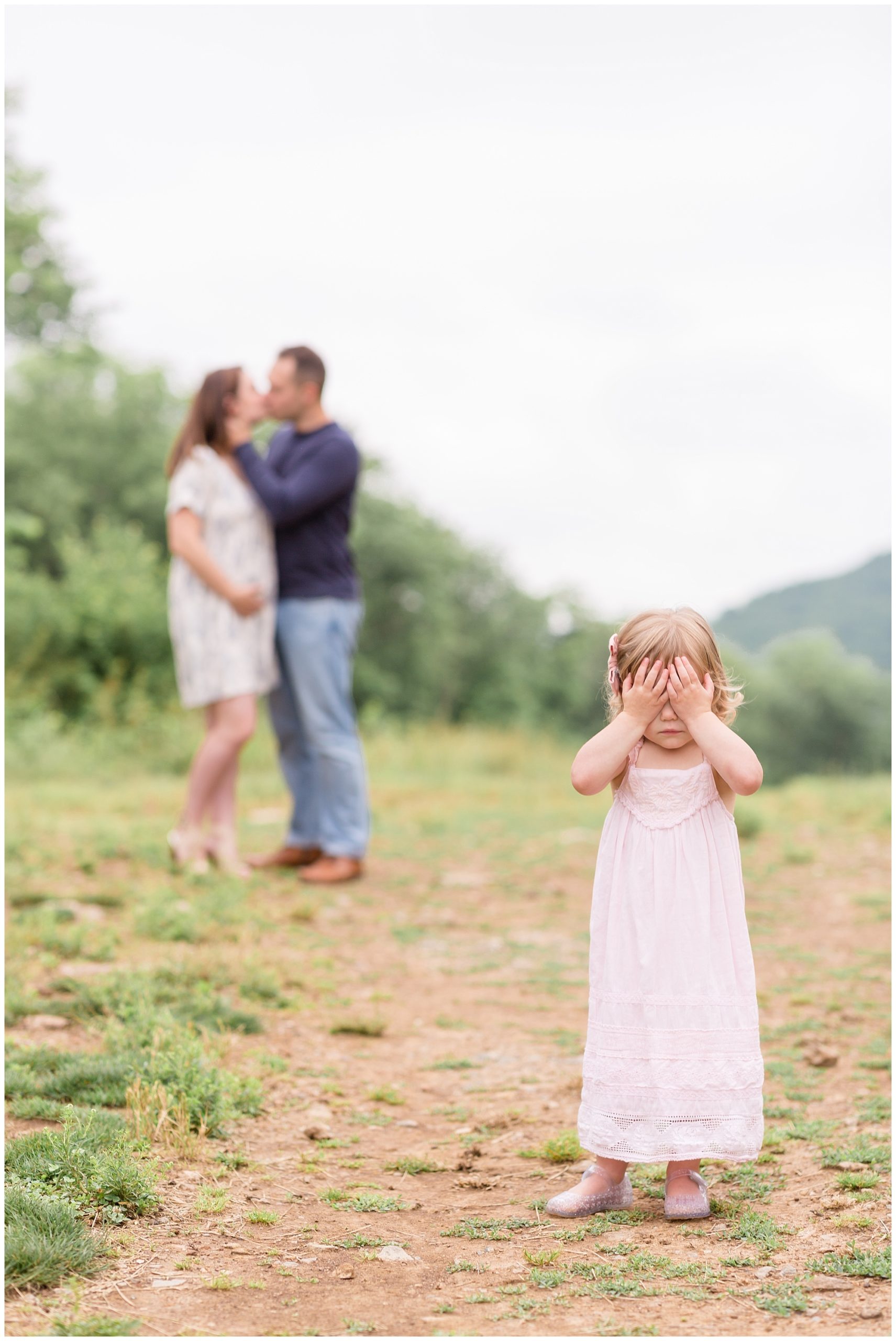 No peeking! This sweet little girl is hiding her eyes while mom and dad steal a kiss. She is wearing a soft pink long dress with lace embellishments and a matching pink bow. This session is featured on our monthly membership called "Behind the Lens". Make sure to check out the blog for more information!