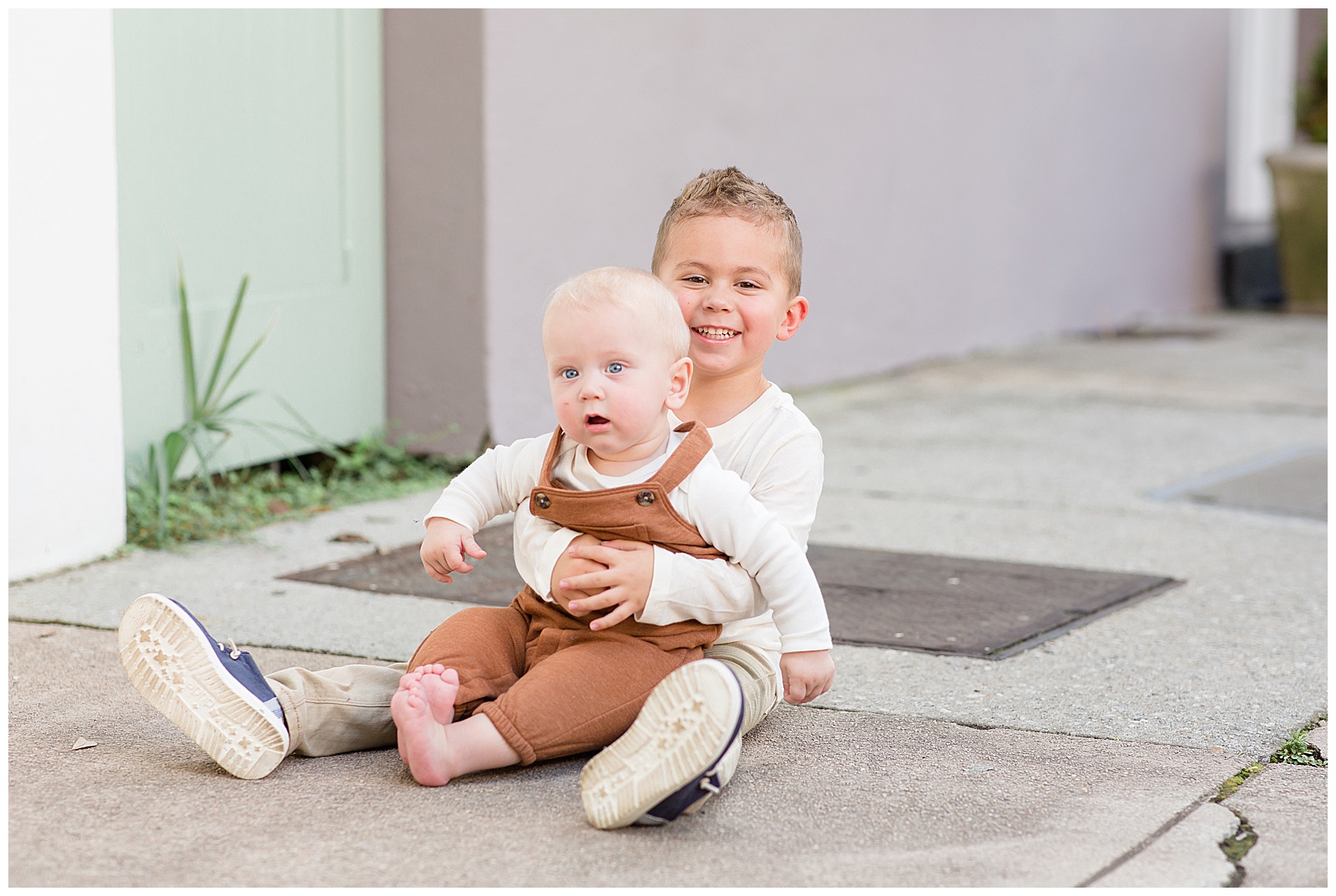Little brothers sit on Rainbow Row in Charleston, SC as the oldest toddler brother holds his baby brother.