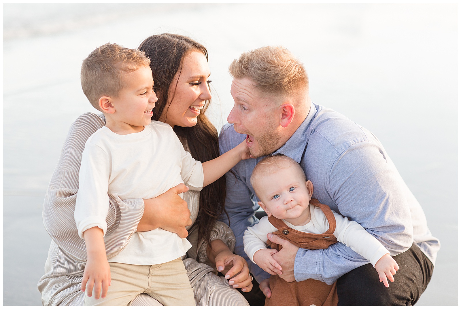 Family squats on the beach as parents hold sons on their knees in Charleston. SC during their family session.