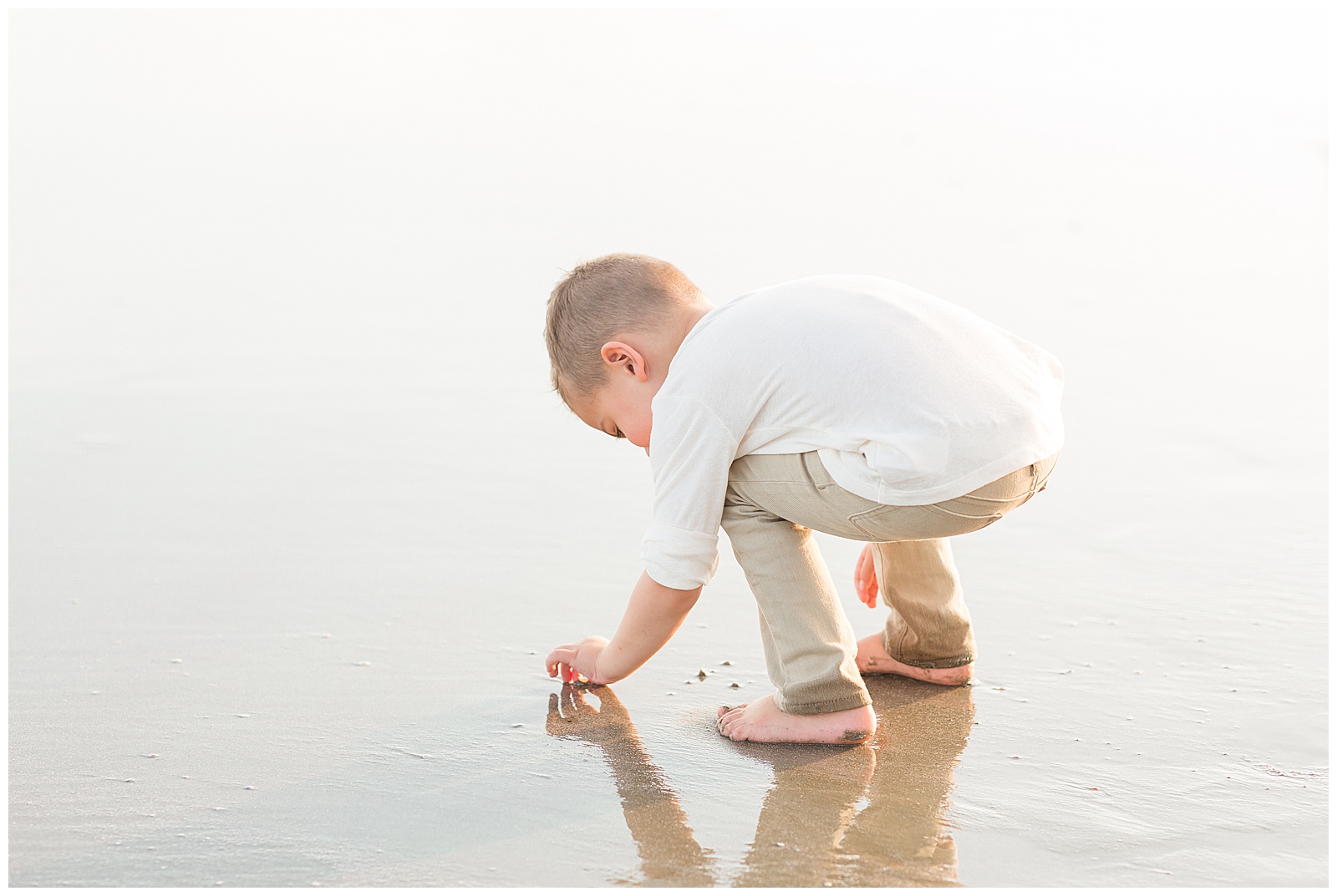 Family photographer, Rebecca Rice, captures toddler boy in his element on the beach picking up shells in the sand along the shoreline.