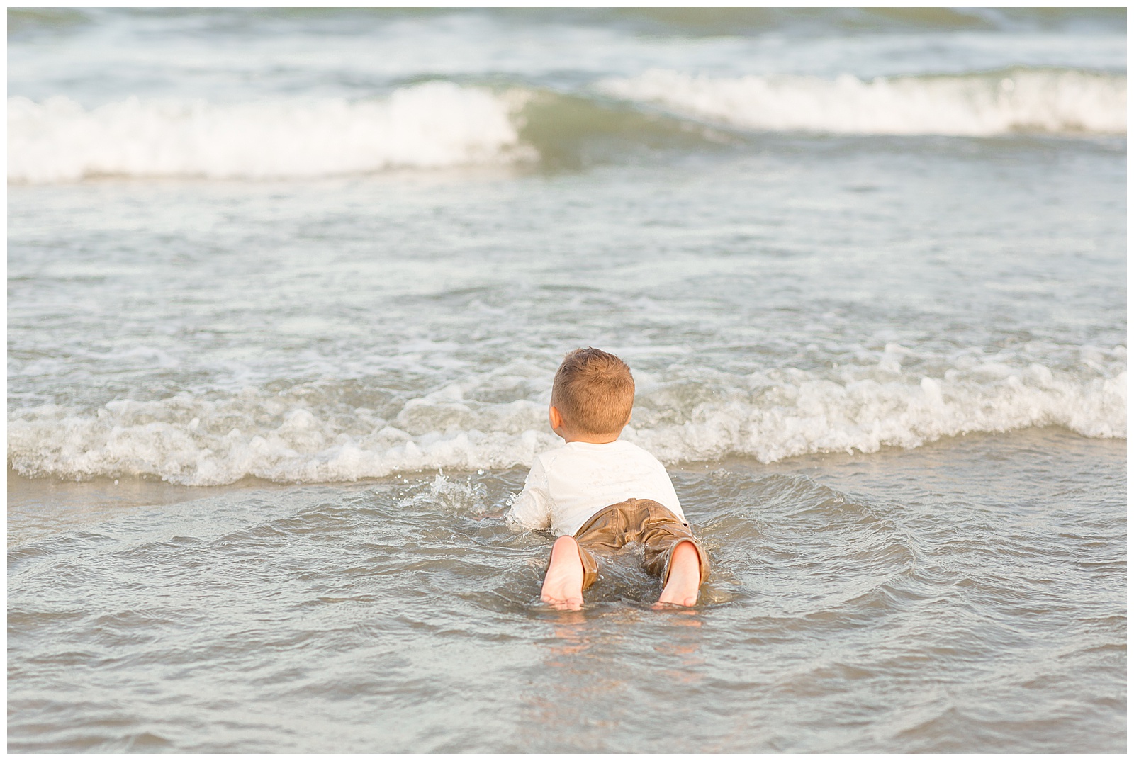 Little boy ends their family photography session with Rebecca Rice Photography as he has waited until the end of the session to get to lay in the Charleston ocean water with his clothes on!