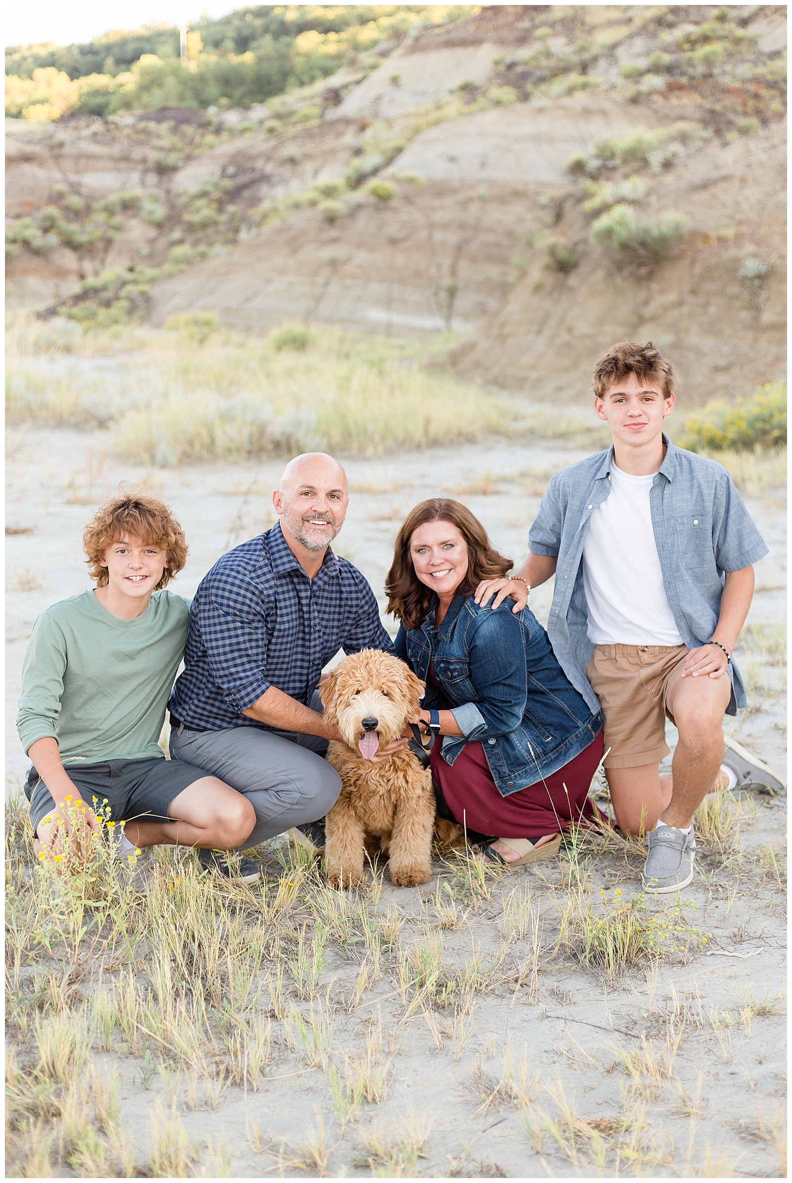 Family smiles with doodle pup, teen boys, mom and dad in the rolling hills of North Dakota for their family photography session with Rebecca Rice Photography for Behind the Lens, a membership course for family photographers. 
