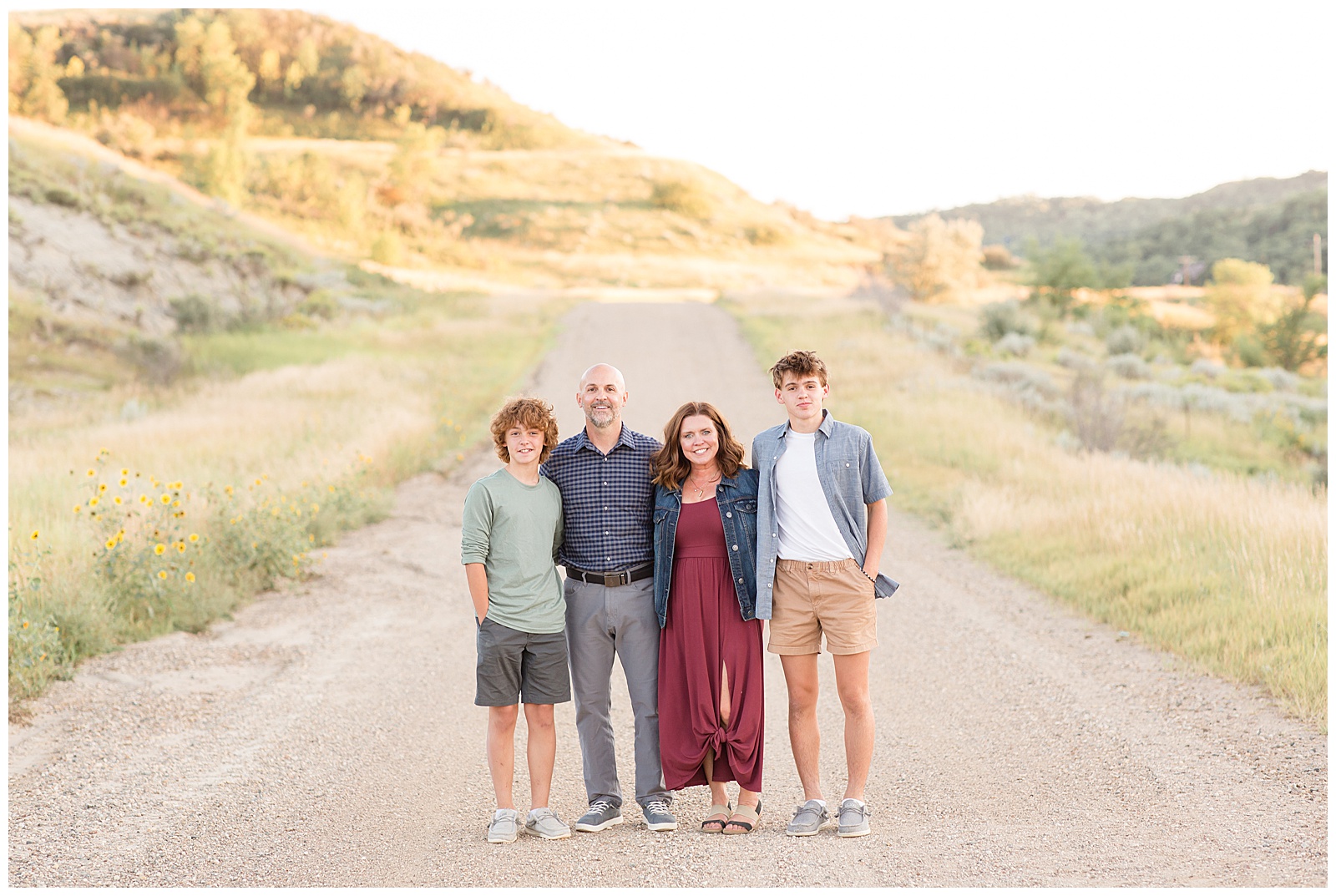 Family of 4 wear coordinating outfits for family photography session with Rebecca Rice Photography wearing green, blue, white, and burgundy colors during golden hour in North Dakota. Behind the Lens is a membership course for family photographers.