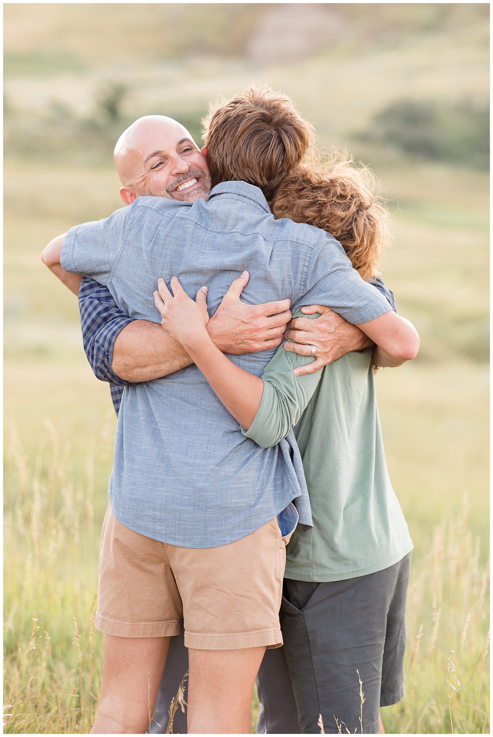 Dad hugs teen sons in the fields of North Dakota mountains during their family session with Rebecca Rice Photography for a course for family photographers.