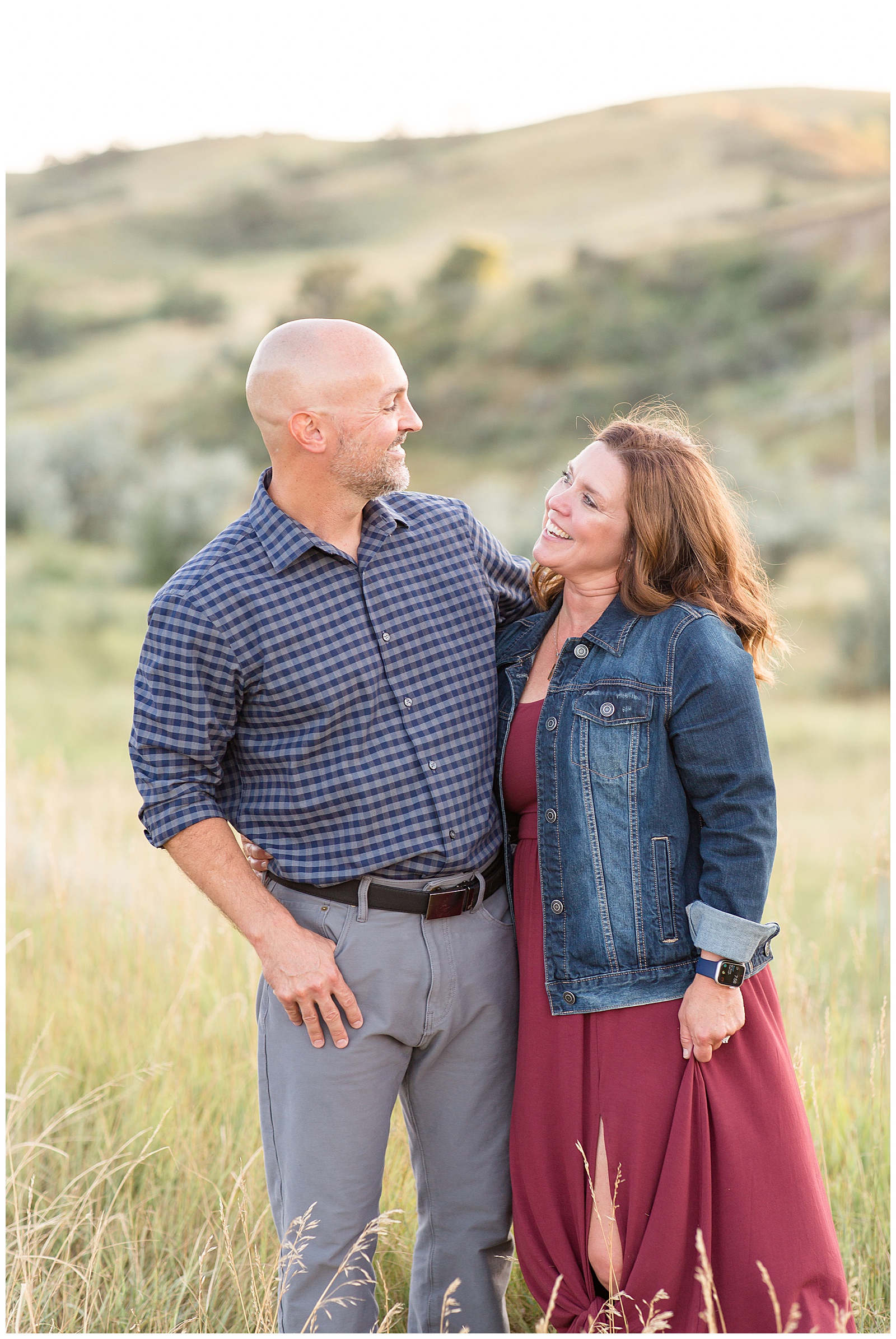 Mom and Dad smile at each other in field of North Dakota hills for family session.