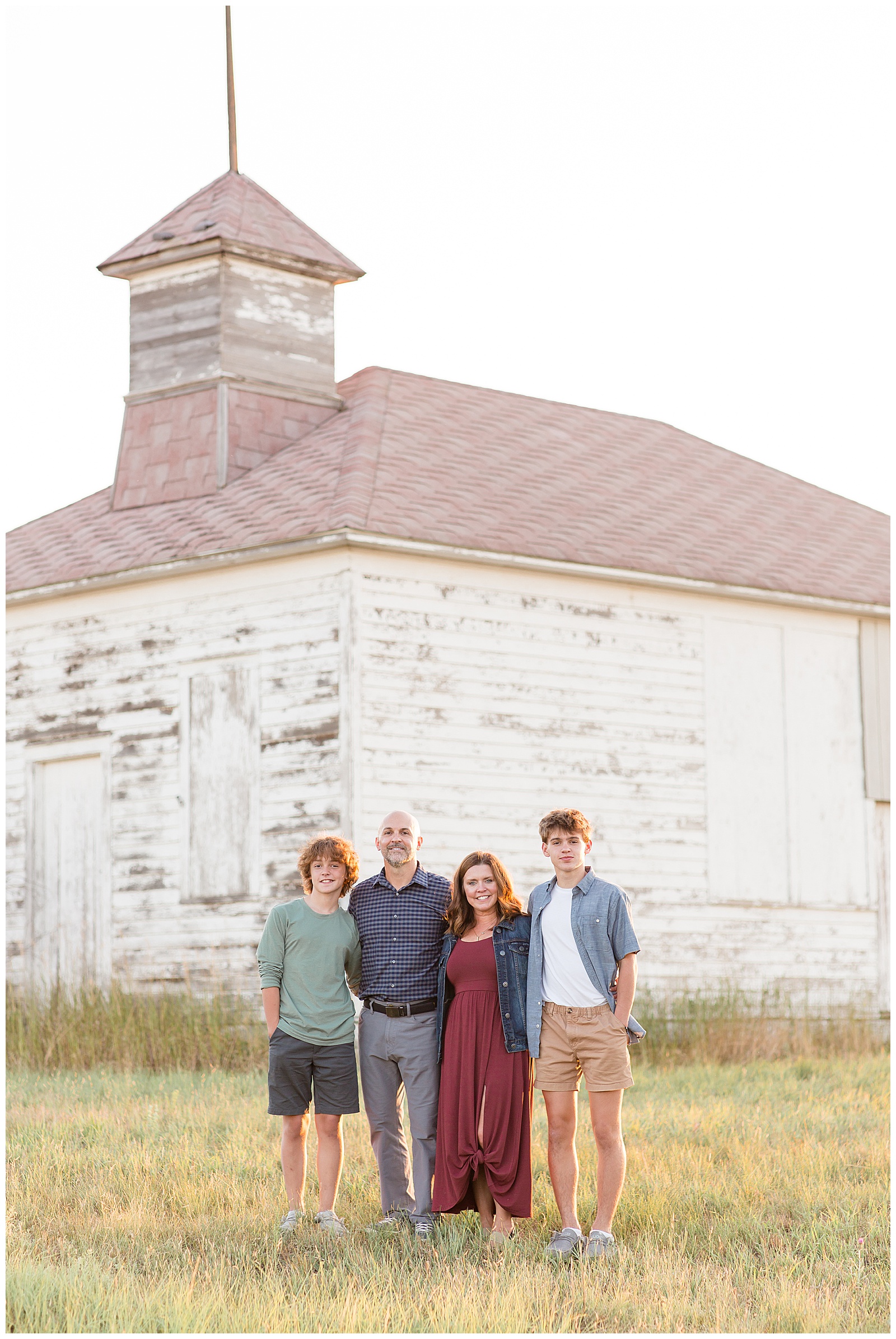 Family of 4, mom and dad, teen boys, stand in front of old building with that golden hour glow taken by Rebecca Rice Photography.